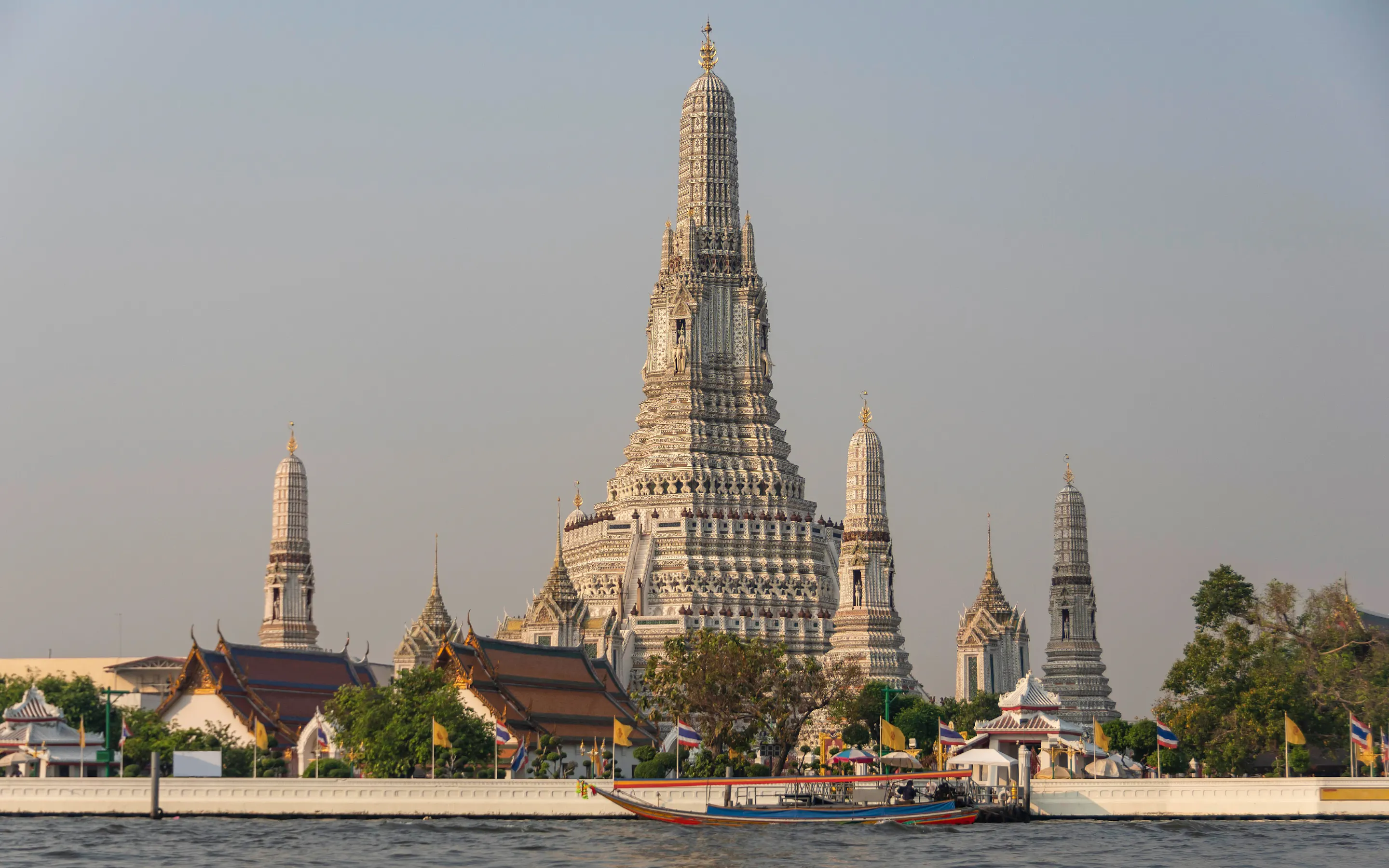 Wat Arun rises above the Chao Phraya River in Bangkok, where a long-tail boat passes the temple frontage.