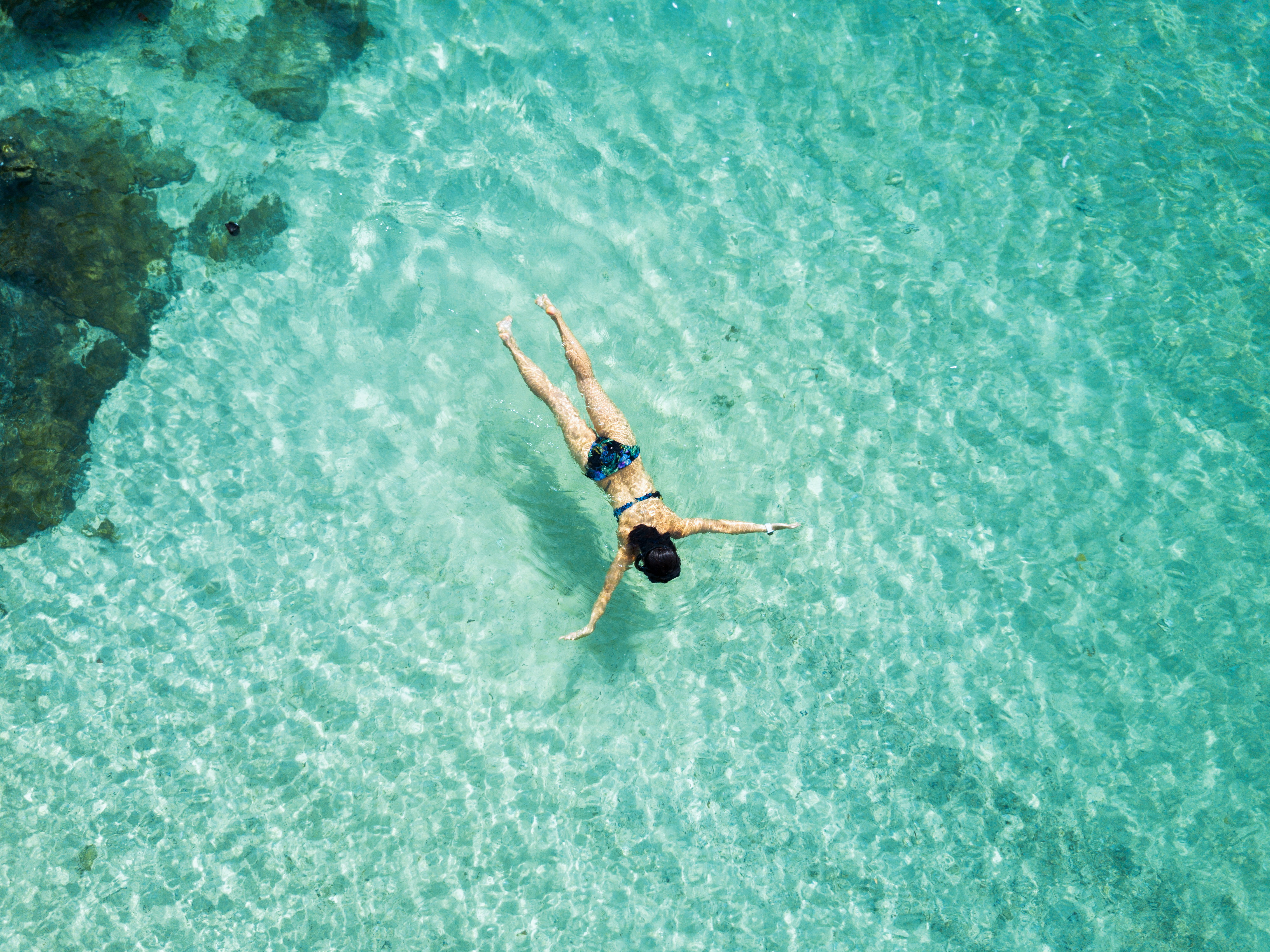 A snorkeler floats above pale coral shadows in clear turquoise water near the islands off Six Senses Yao Noi.