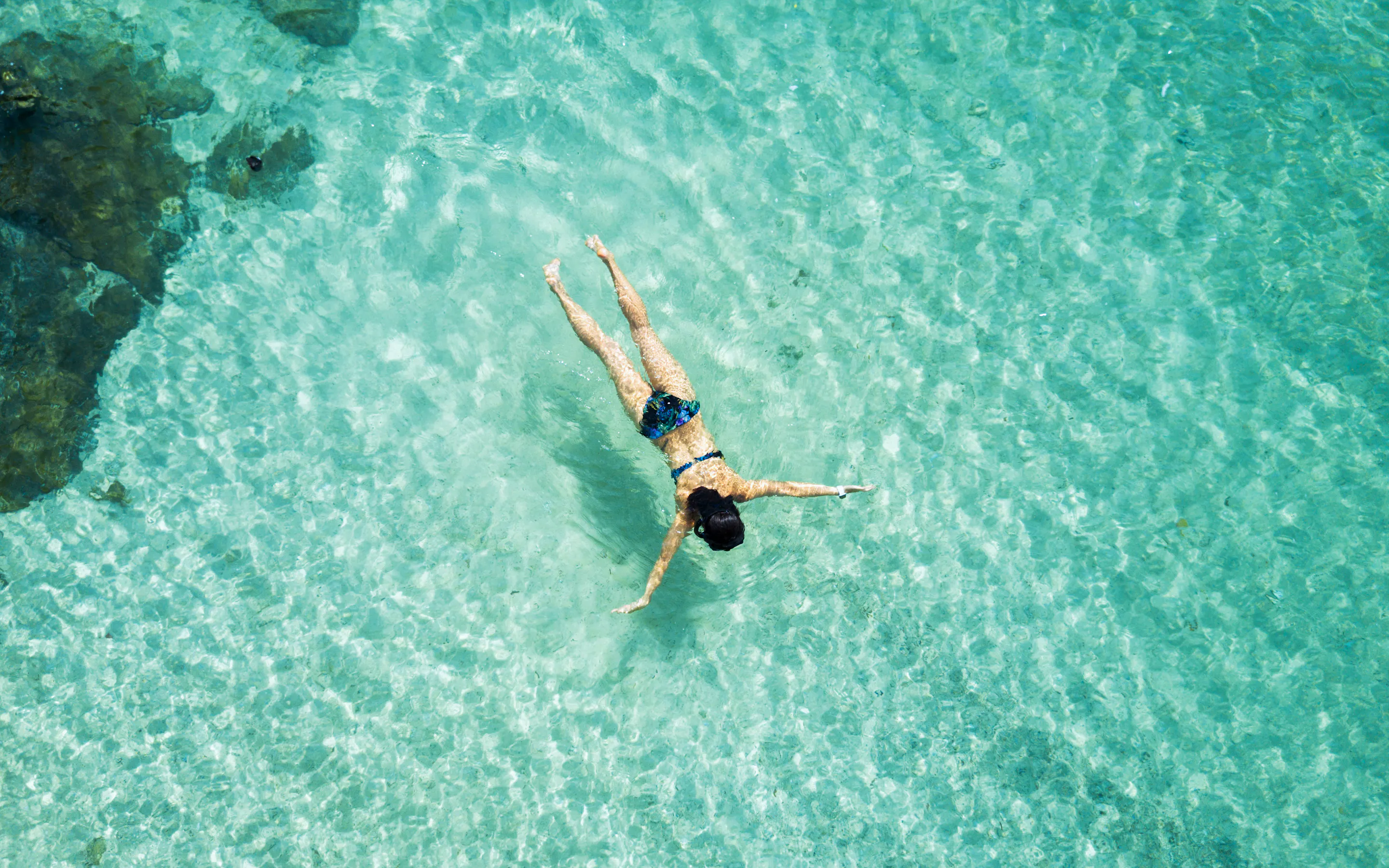A snorkeler floats above pale coral shadows in clear turquoise water near the islands off Six Senses Yao Noi.