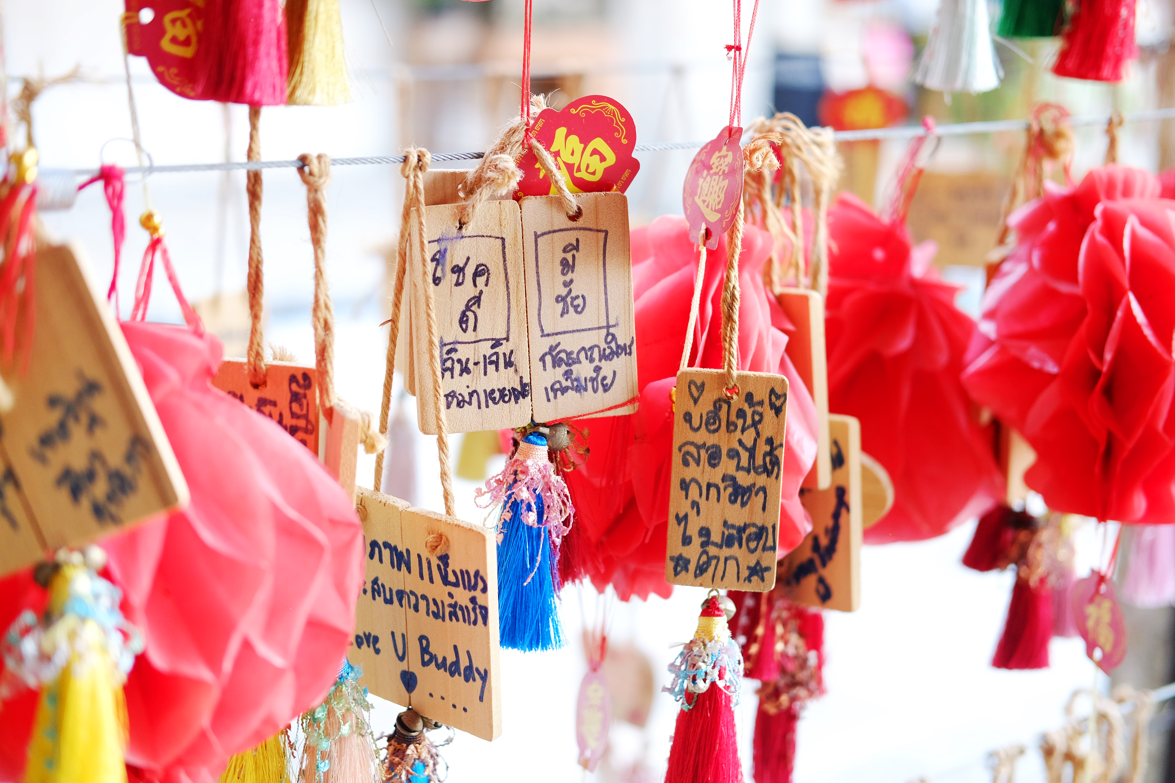 Wooden prayer plaques and red tassels hang in soft light, with handwritten messages filling the narrow tags.