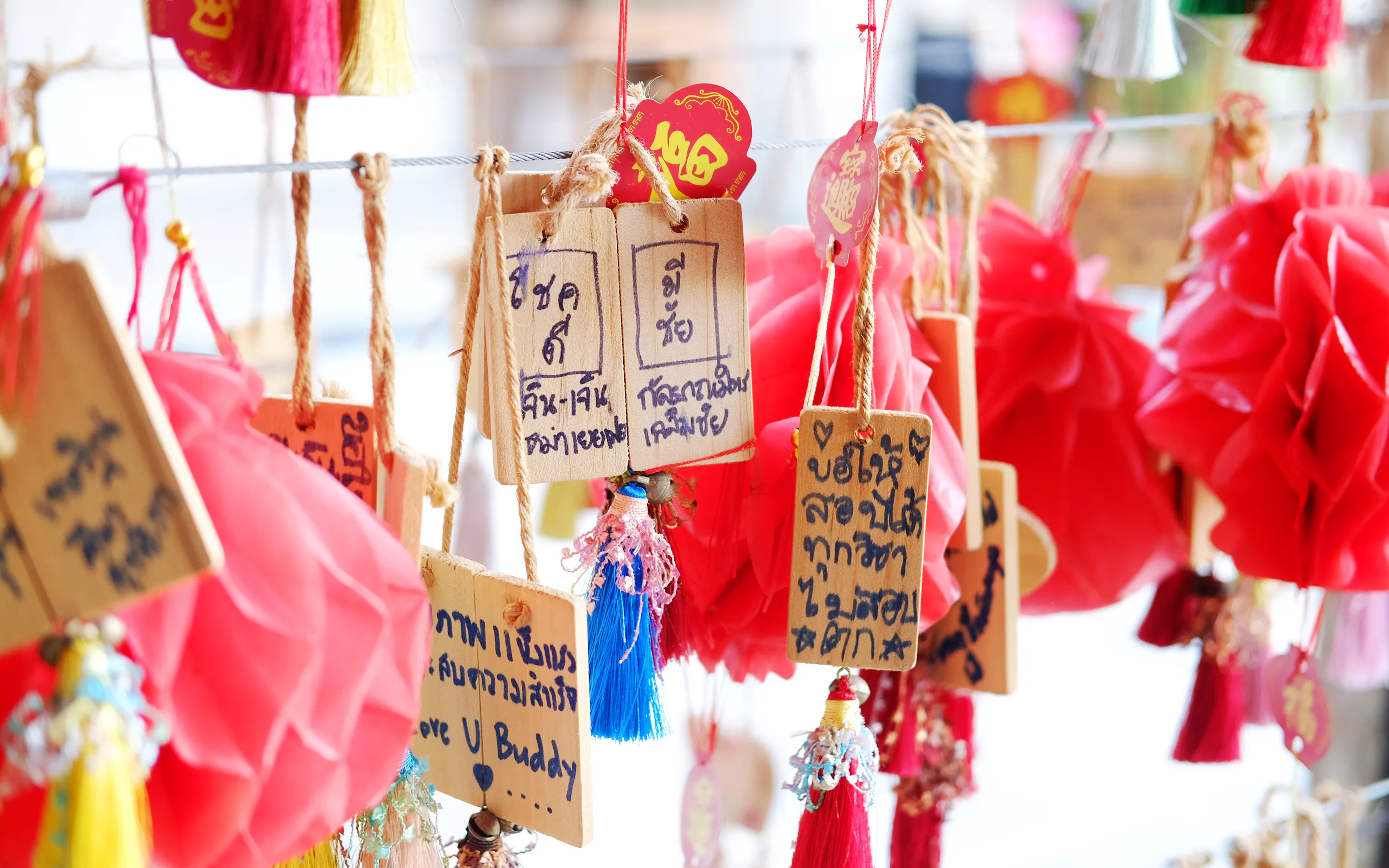 Wooden prayer plaques and red tassels hang in soft light, with handwritten messages filling the narrow tags.