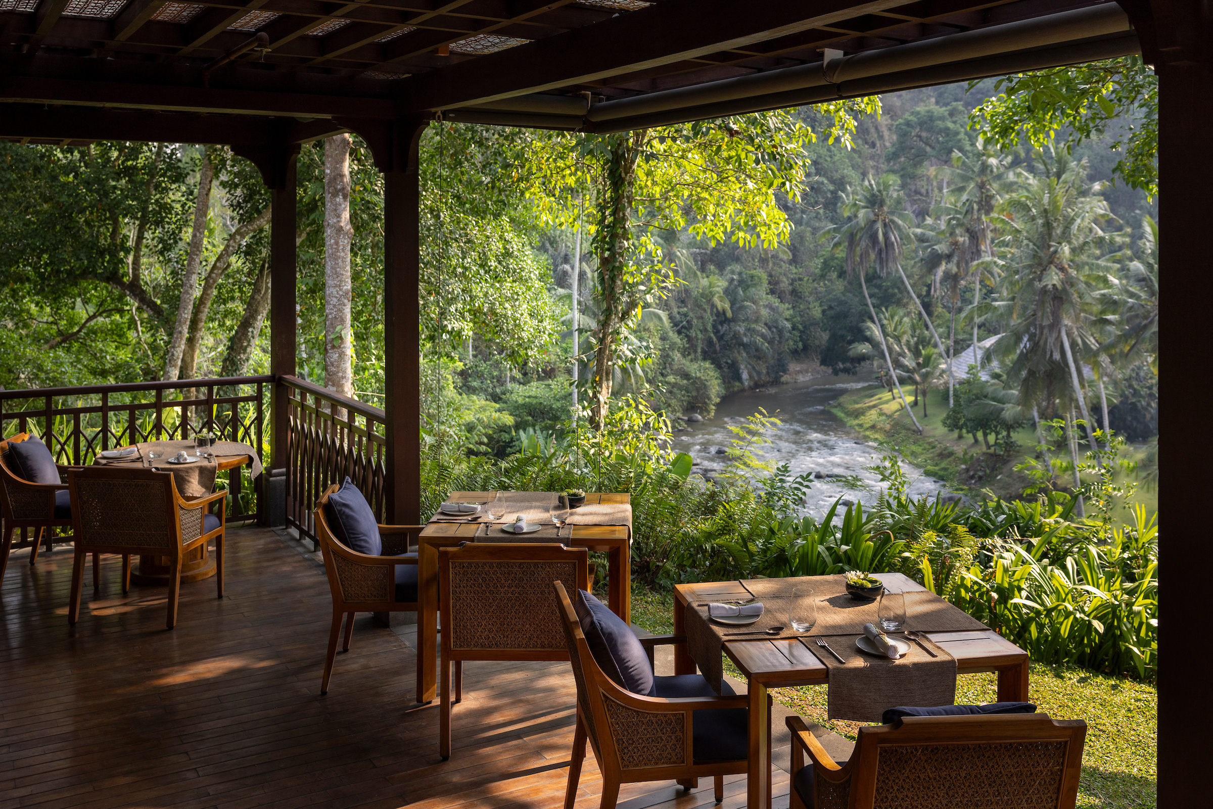 Set tables look across a river valley from Mandapa's Sawah Terrace, where palms and jungle crowd the opposite bank.