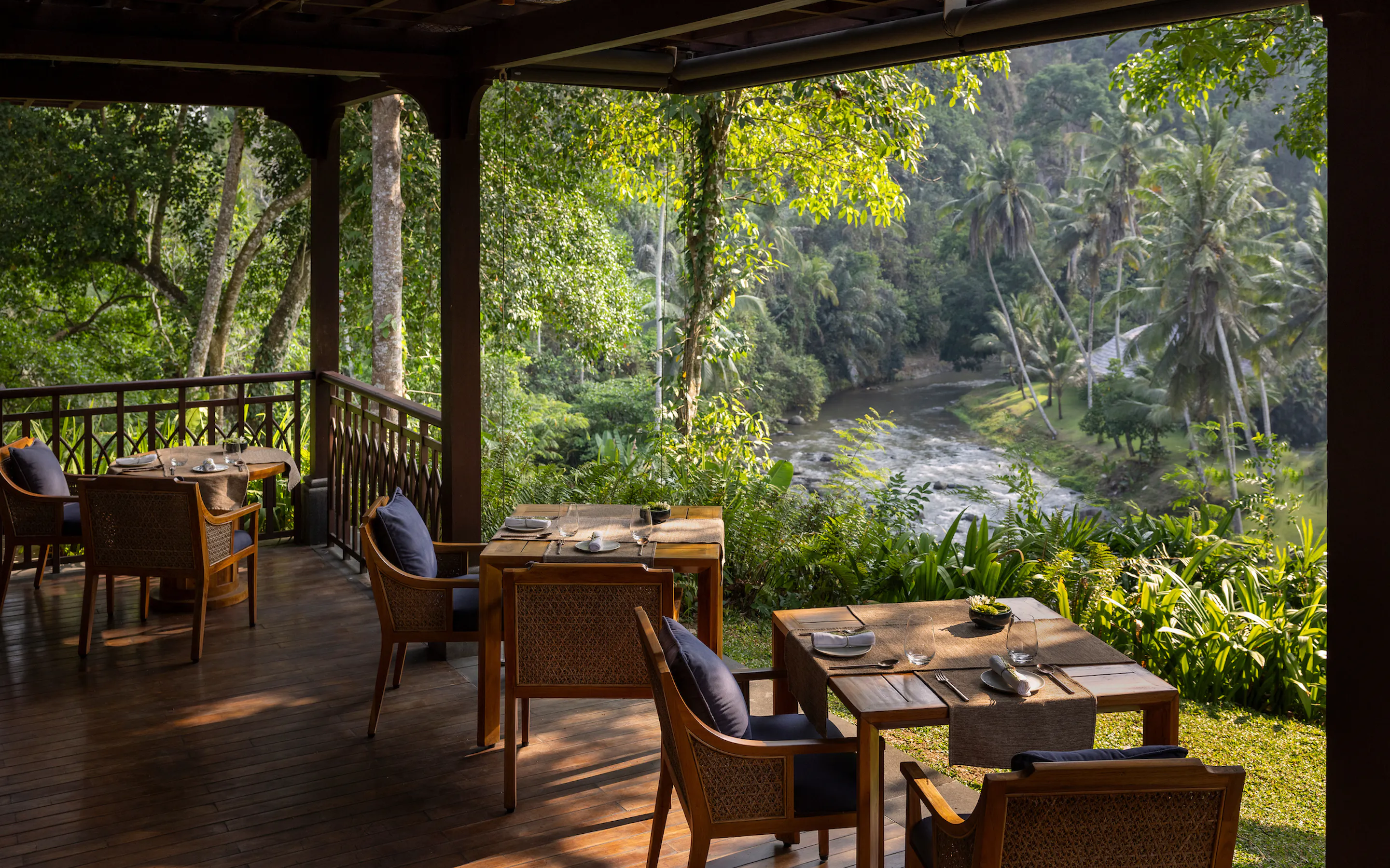 Set tables look across a river valley from Mandapa's Sawah Terrace, where palms and jungle crowd the opposite bank.