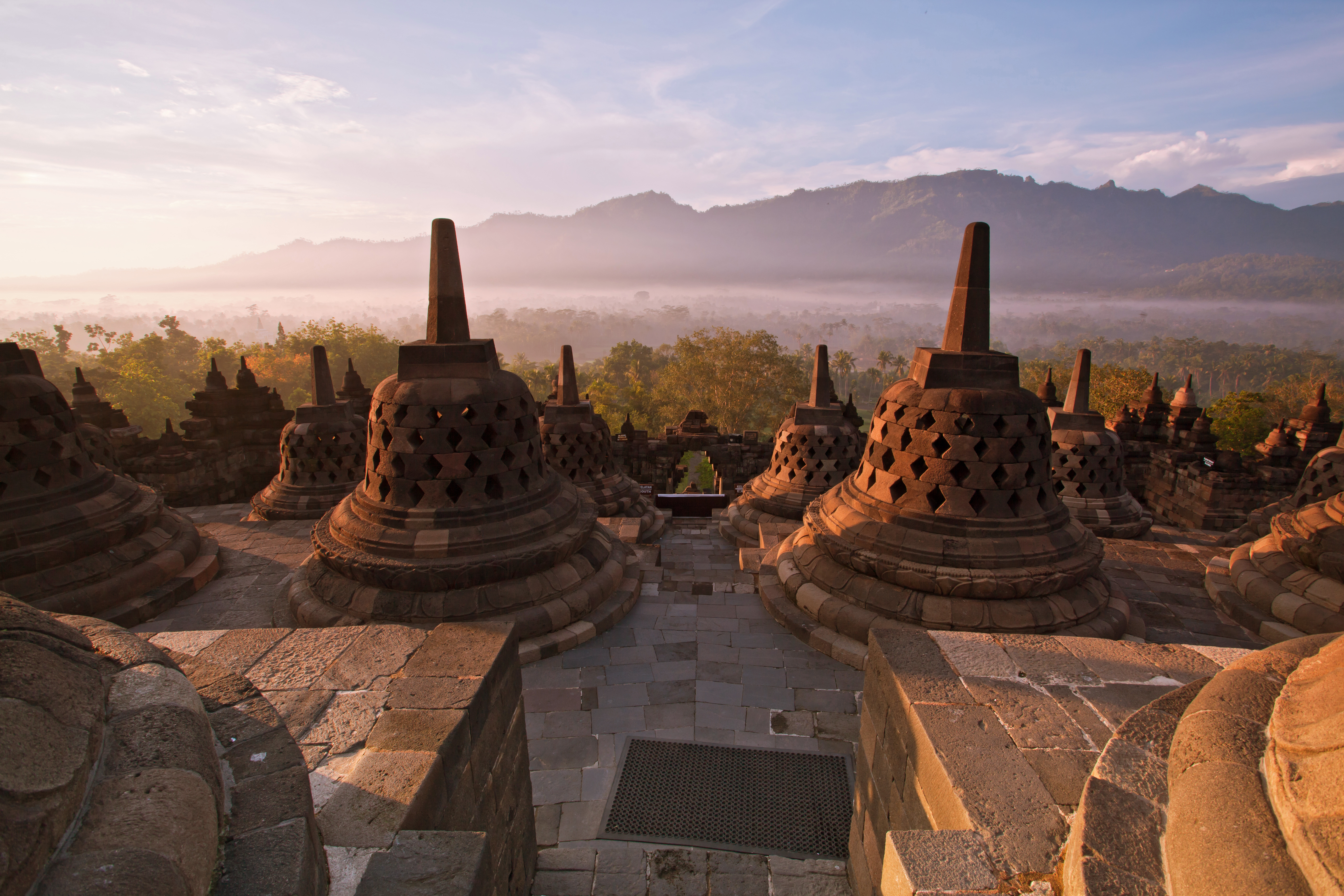 Borobudur's stone stupas catch the morning sun above a misty plain, with dark mountain ridges rising beyond them.