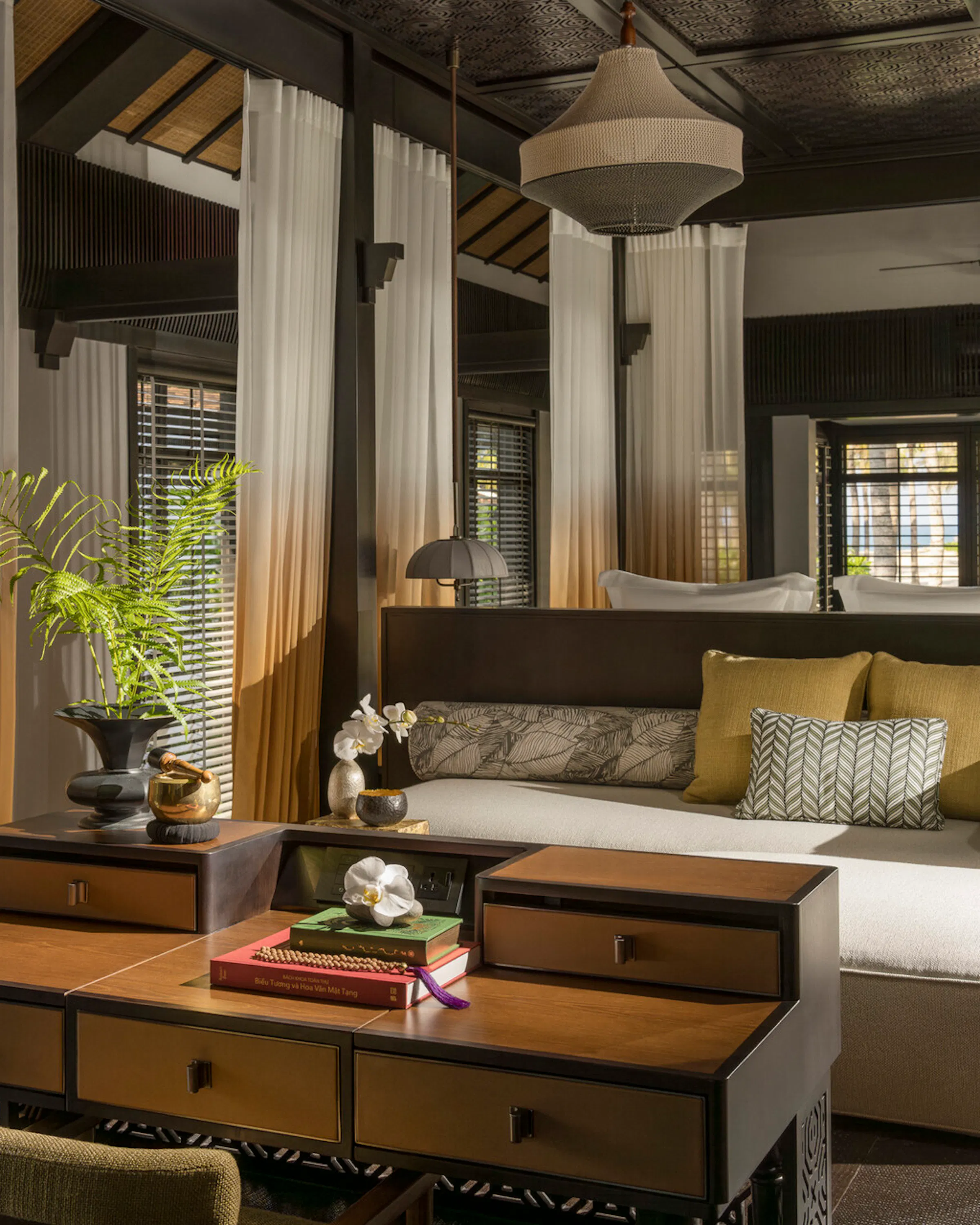 Sunlight falls through sheer curtains onto a daybed and desk inside a dark wood suite at Four Seasons The Nam Hai.