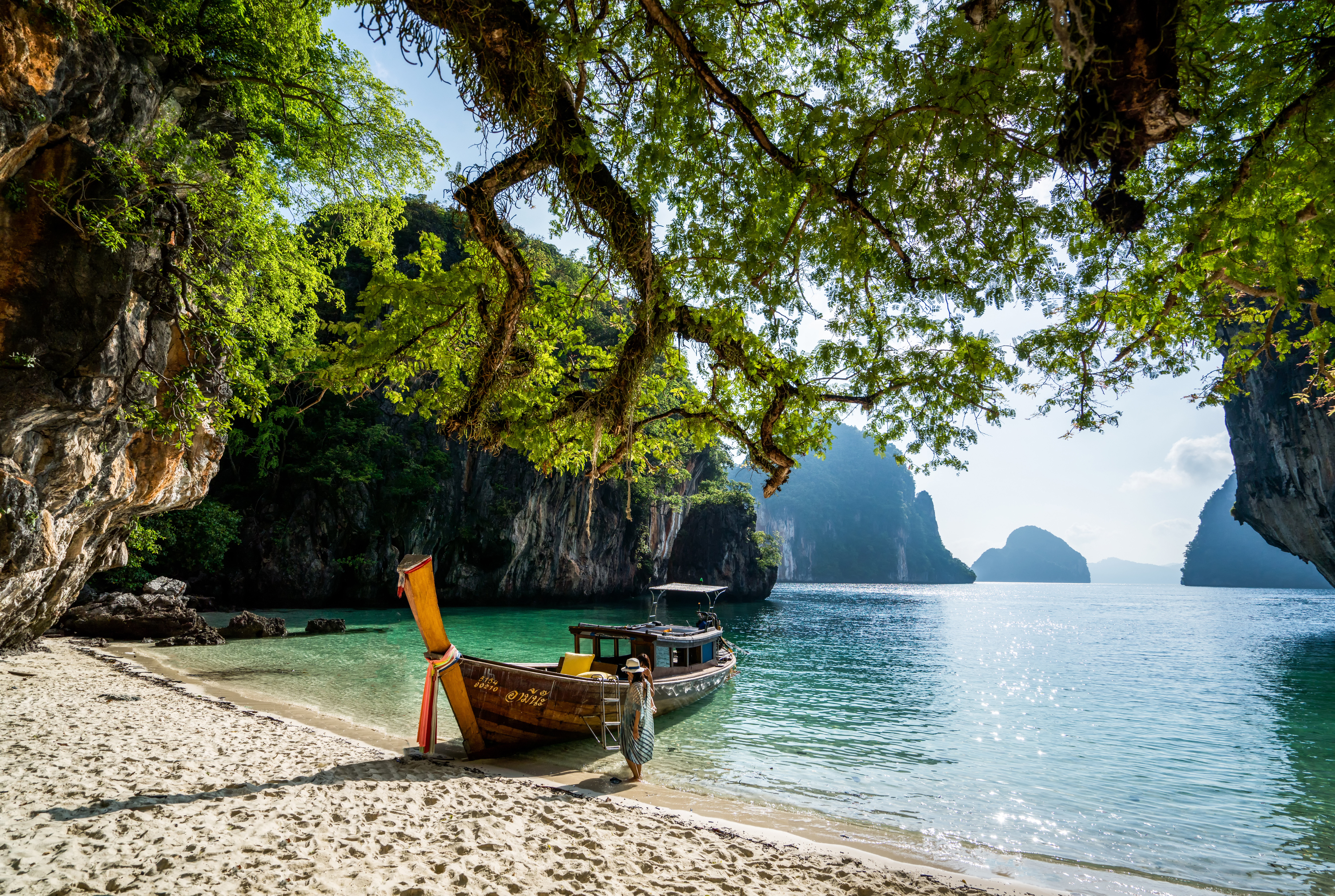 A longtail boat rests on a quiet beach framed by limestone cliffs and calm blue water in Thailand's Phi Phi Islands.