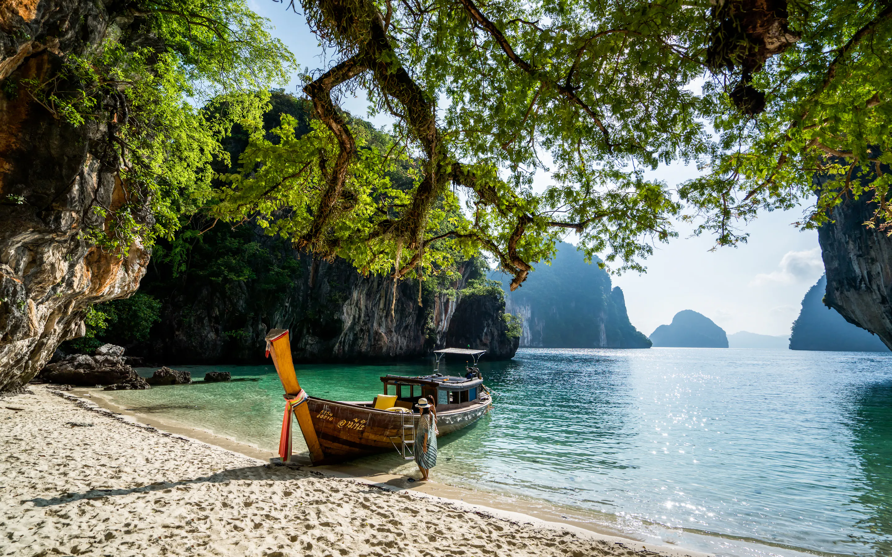 A longtail boat rests on a quiet beach framed by limestone cliffs and calm blue water in Thailand's Phi Phi Islands.