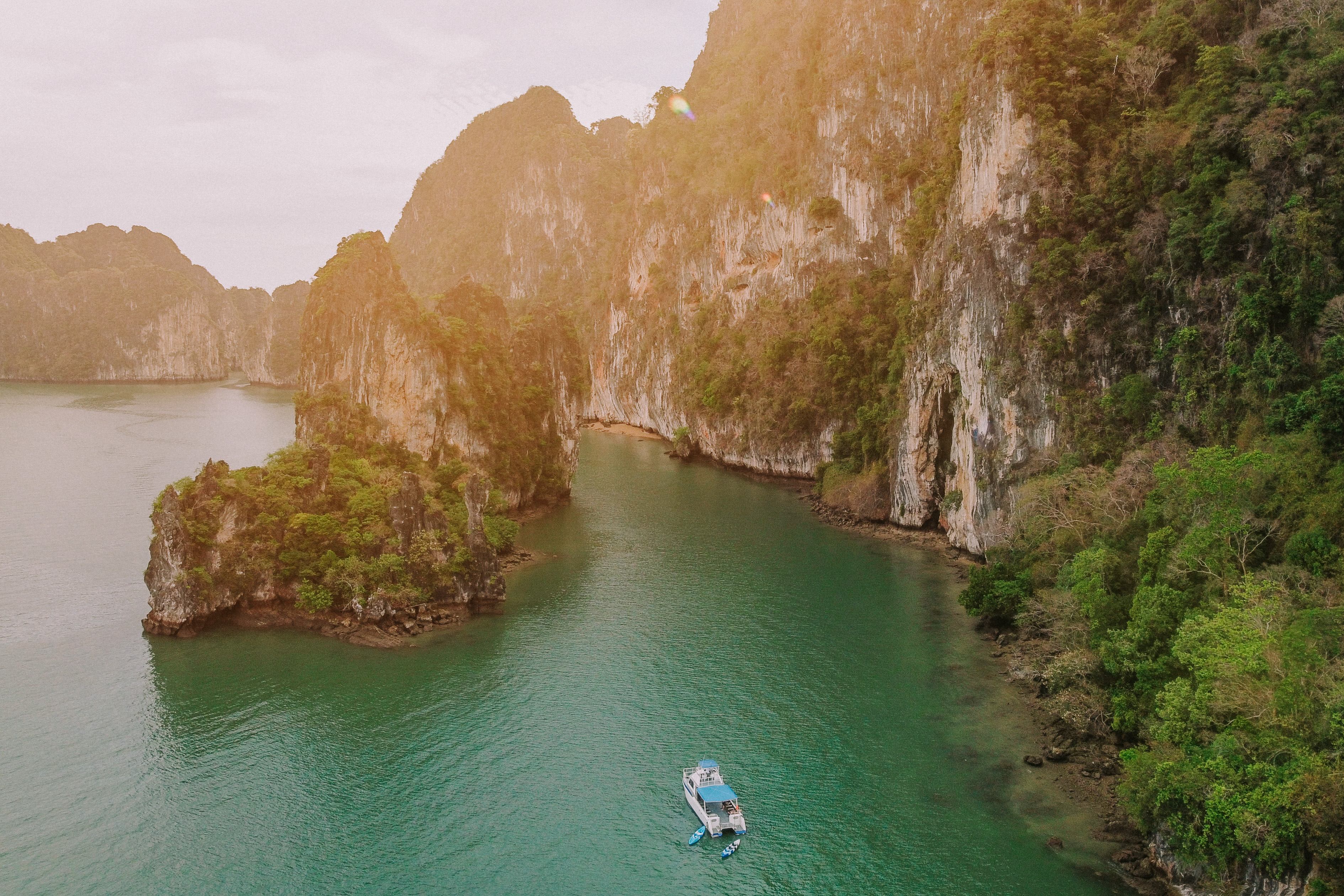 A small white boat floats in emerald water below steep limestone cliffs at Talabeng Island on Thailand's coast.