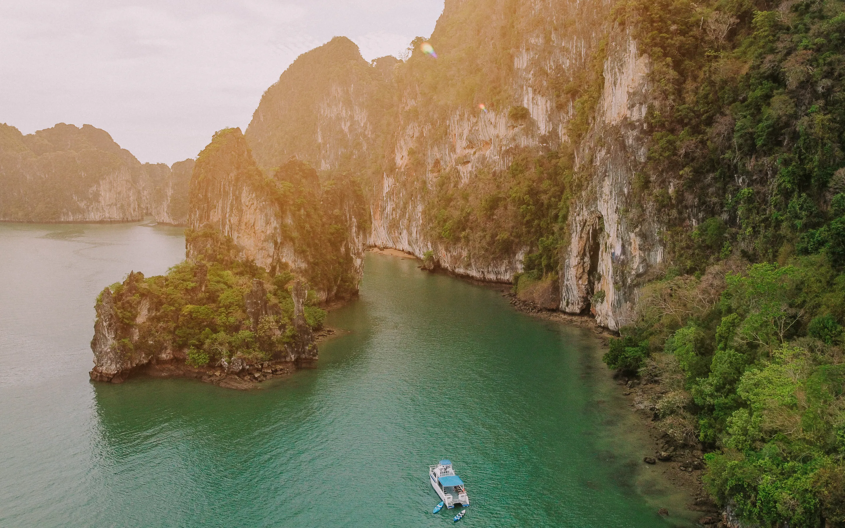A small white boat floats in emerald water below steep limestone cliffs at Talabeng Island on Thailand's coast.
