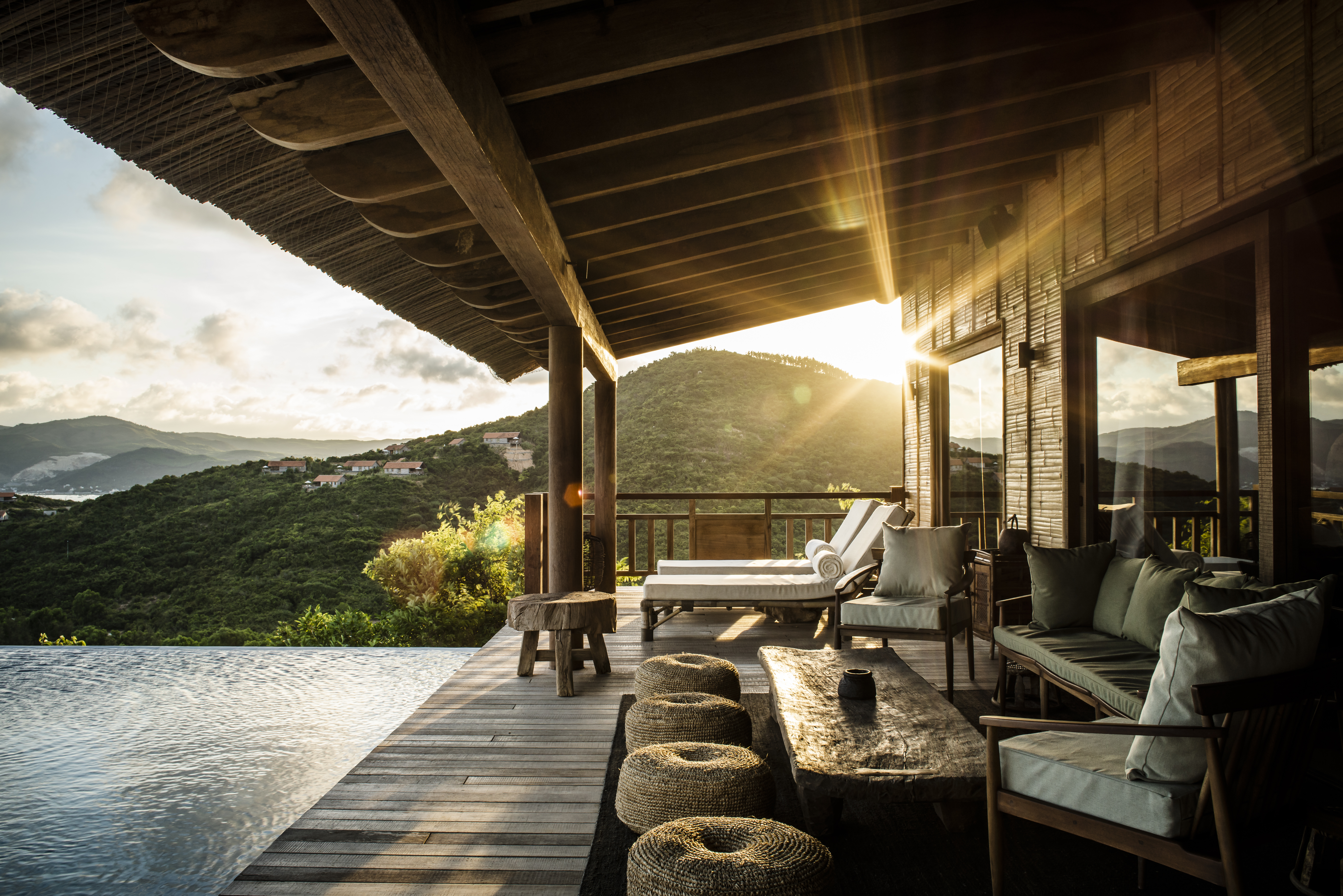 Sunlight pours across Zannier Bãi San Hô's pool villa terrace, where cushioned seats overlook hills and an infinity pool.