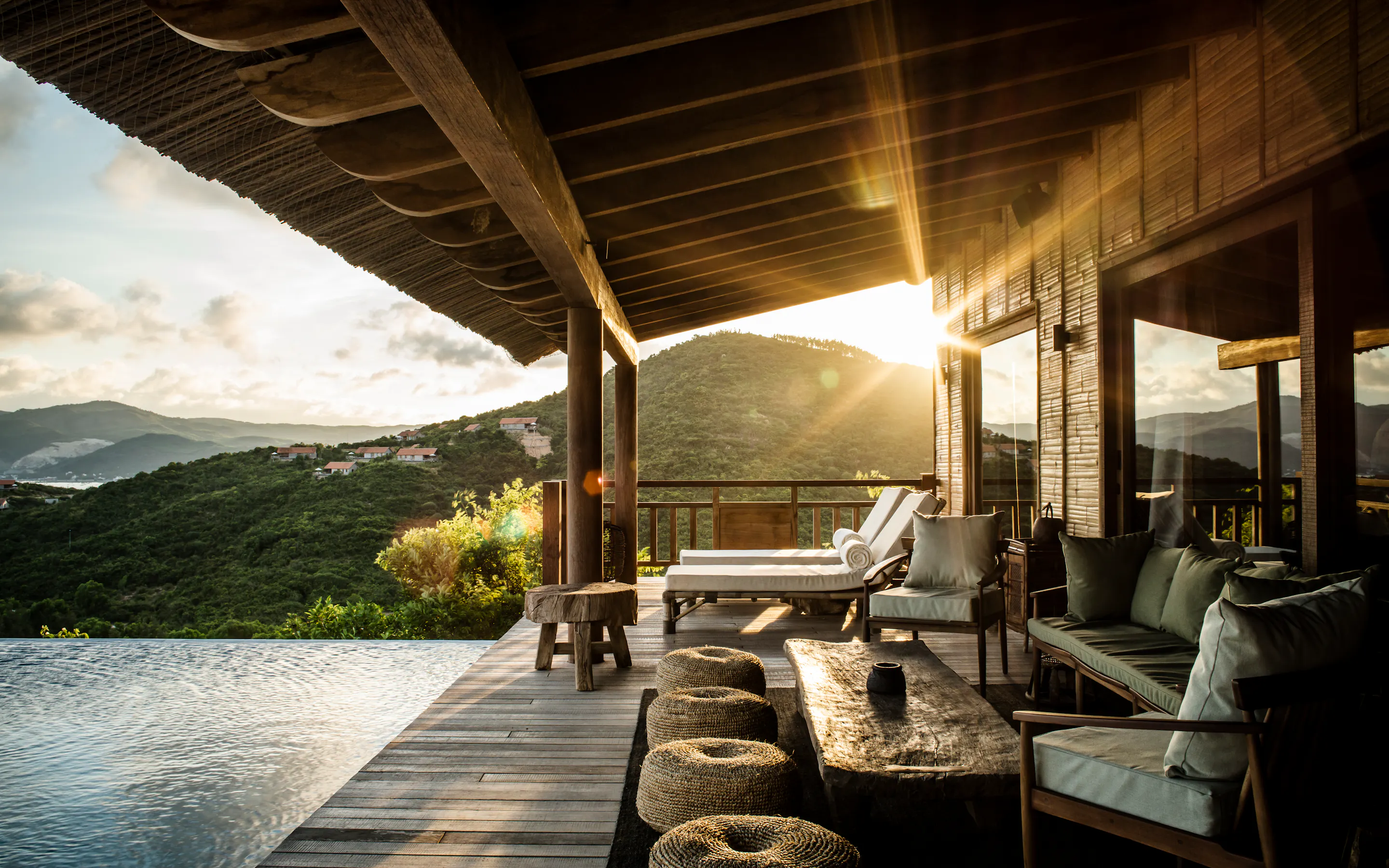 Sunlight pours across Zannier Bãi San Hô's pool villa terrace, where cushioned seats overlook hills and an infinity pool.