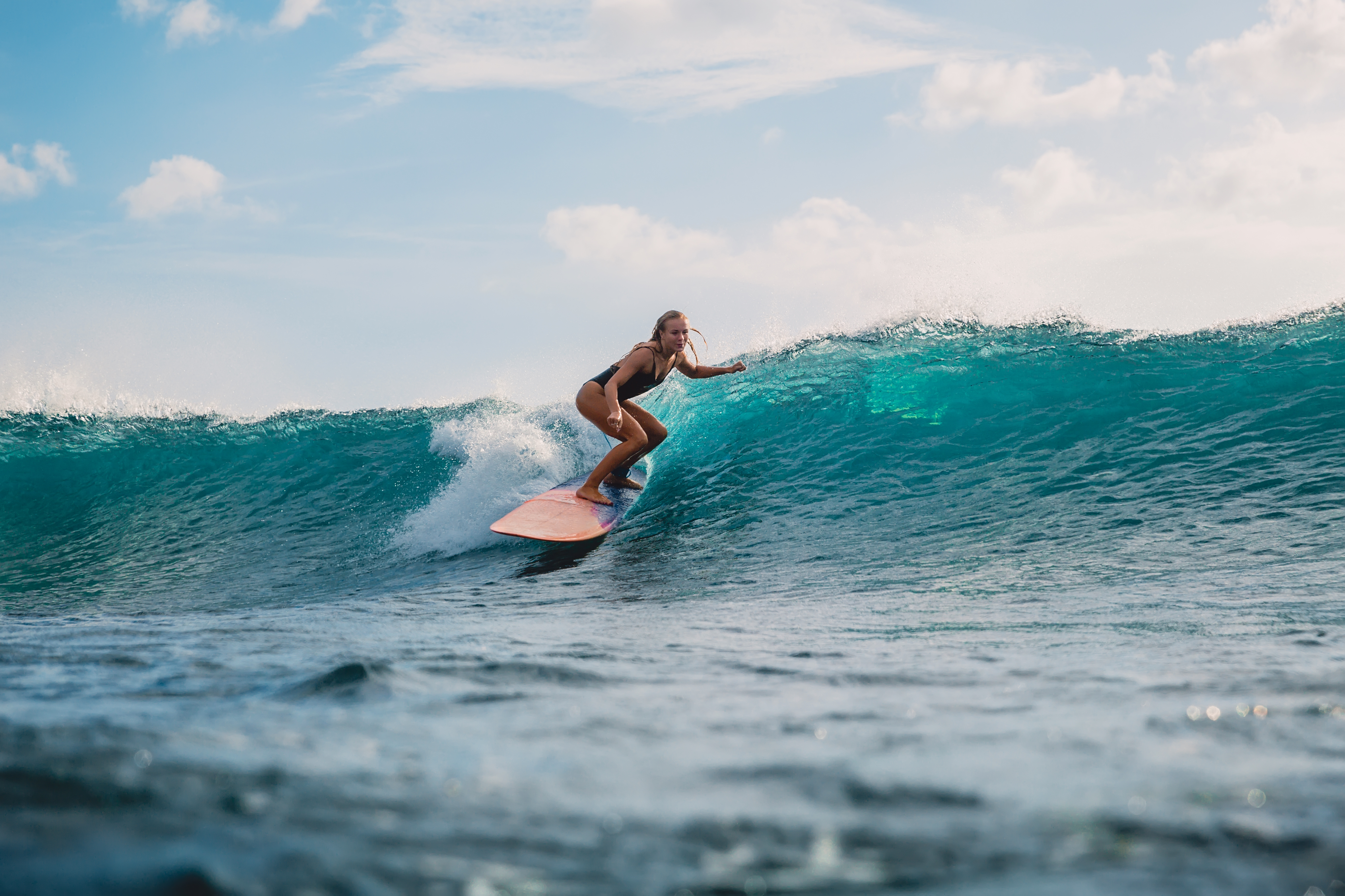 A surfer leans into a bright turquoise wave in Indonesia, with white spray curling across the sunlit water.