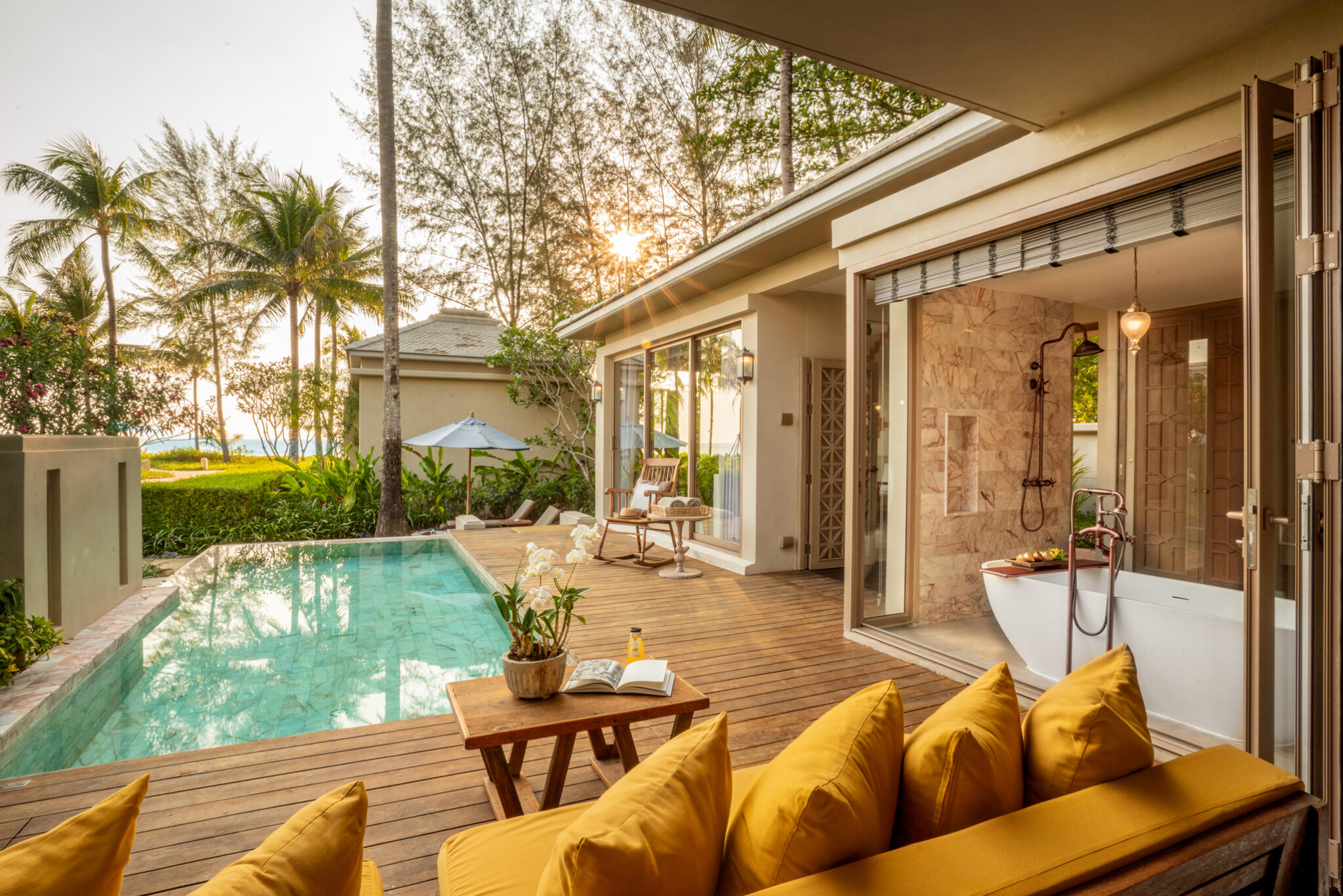 A private pool and open-air bath sit beside a bright villa at Devasom Khao Lak, framed by palms and soft sunlight.