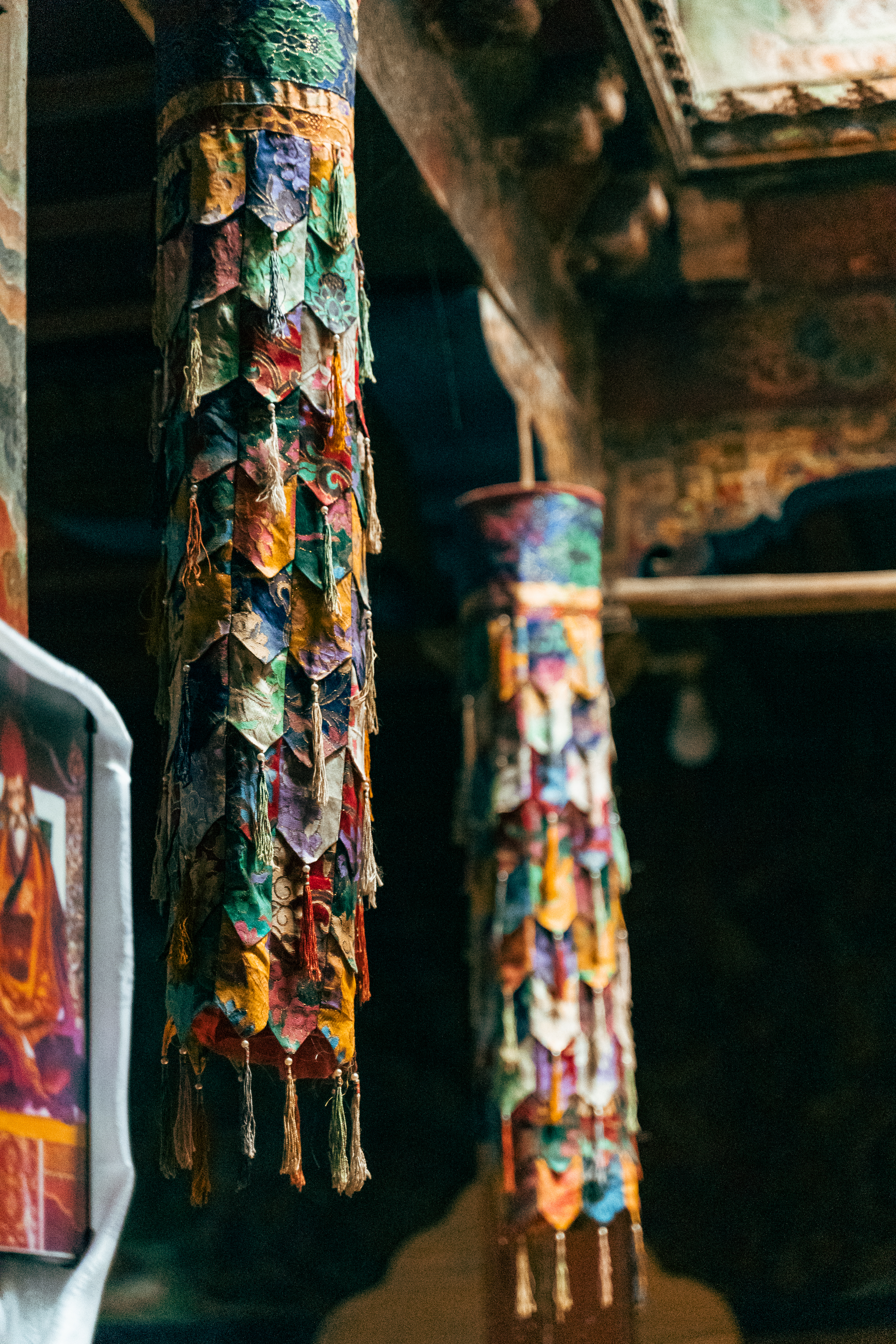 Colorful prayer banners hang inside a dim temple space, with worn wood beams and painted surfaces fading behind.