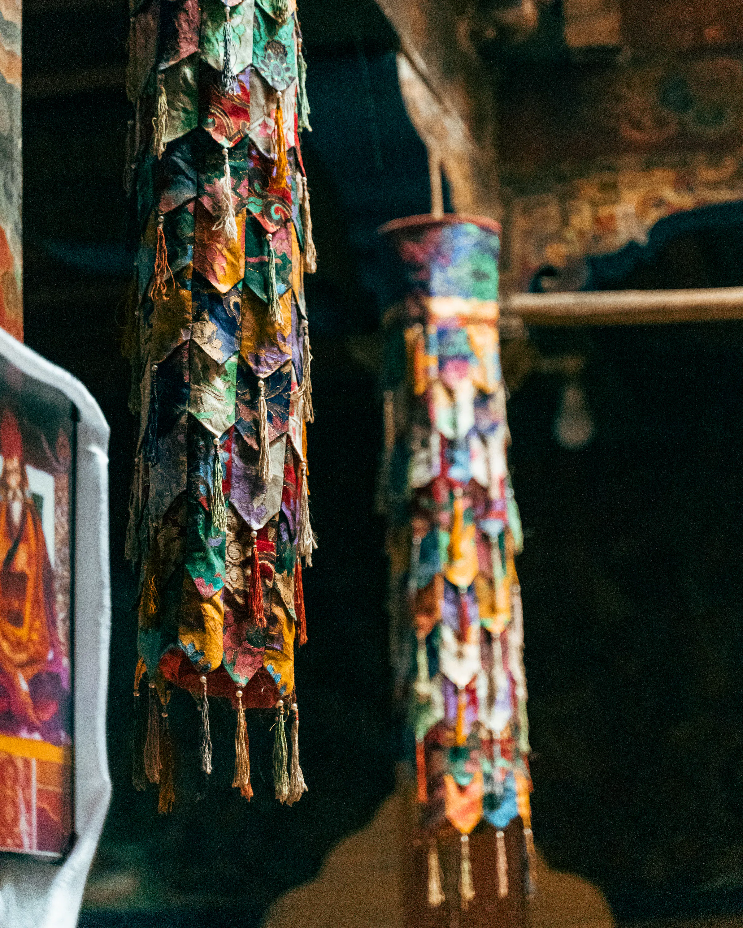 Colorful prayer banners hang inside a dim temple space, with worn wood beams and painted surfaces fading behind.