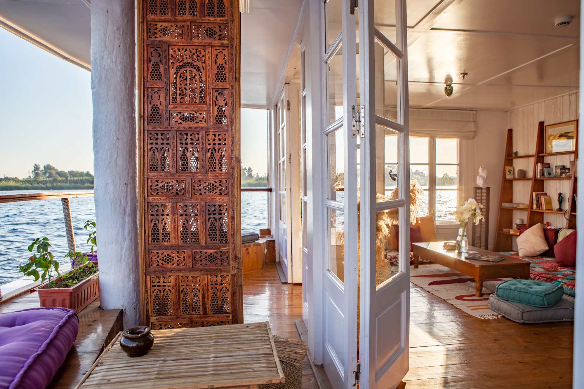 A carved screen opens to a bright library lounge on the lower deck, with river views, bookshelves, and soft seating.