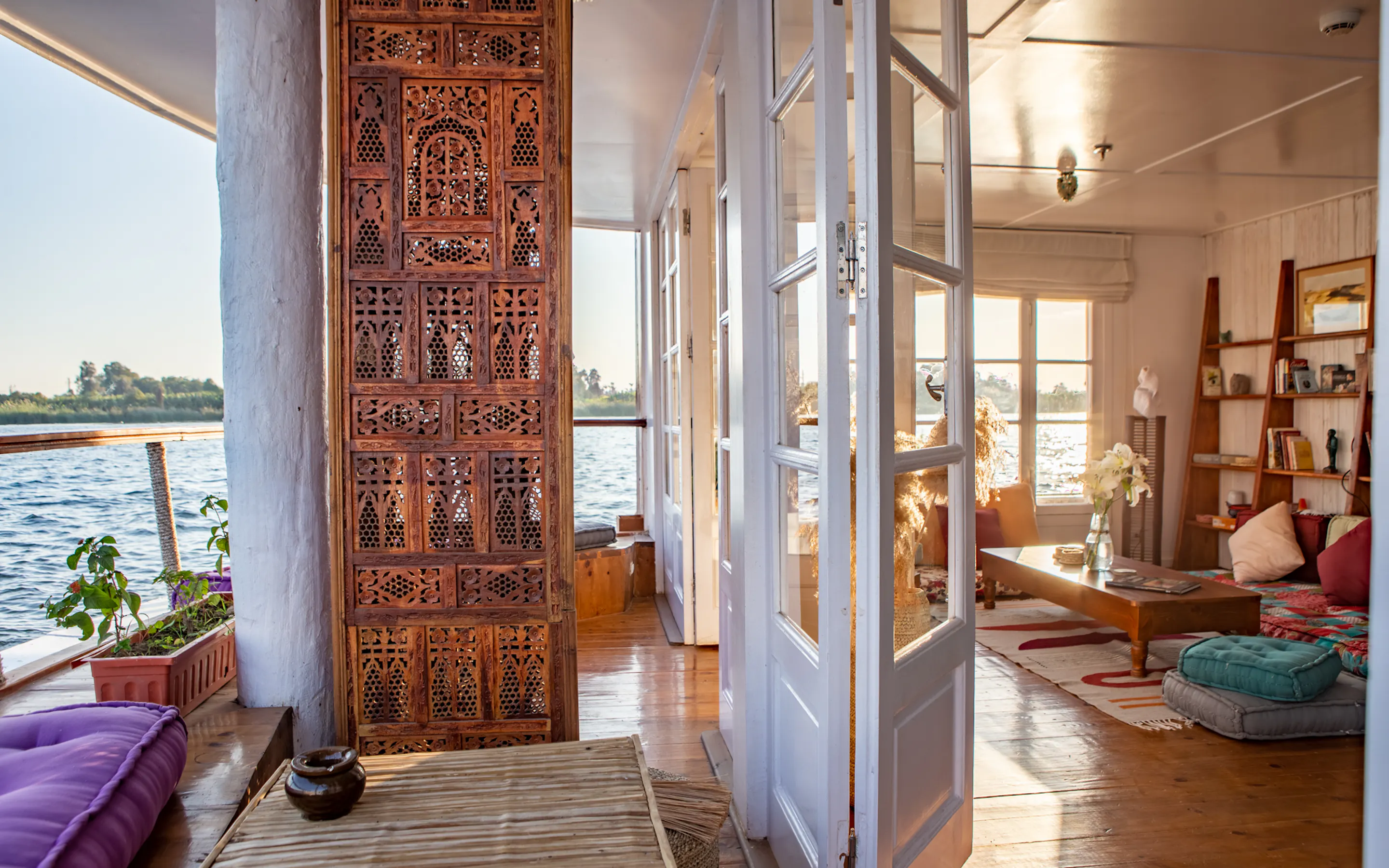A carved screen opens to a bright library lounge on the lower deck, with river views, bookshelves, and soft seating.