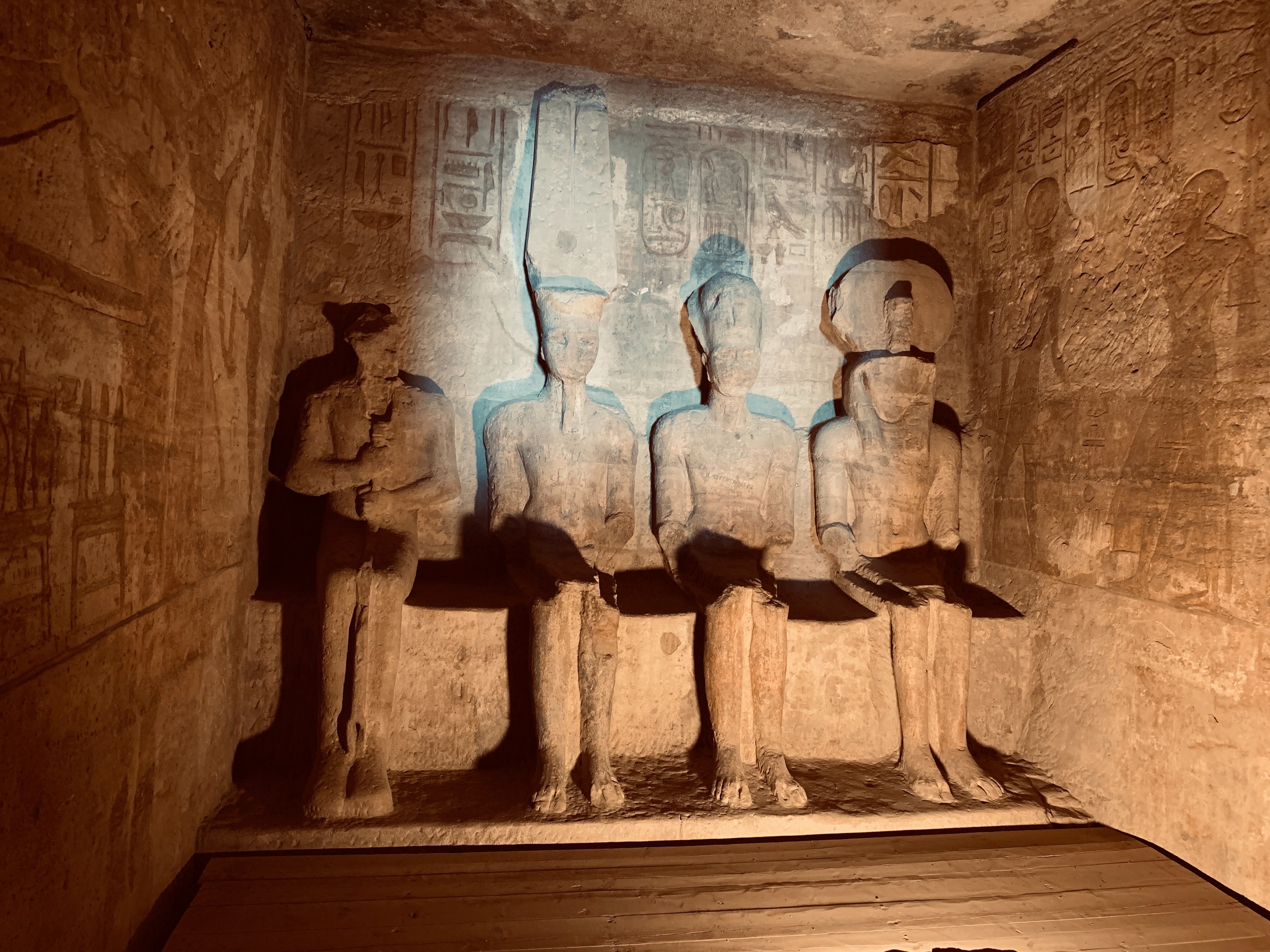 Four carved figures sit inside a dim stone chamber at Karnak in Luxor, with etched walls and warm spotlighted reliefs.