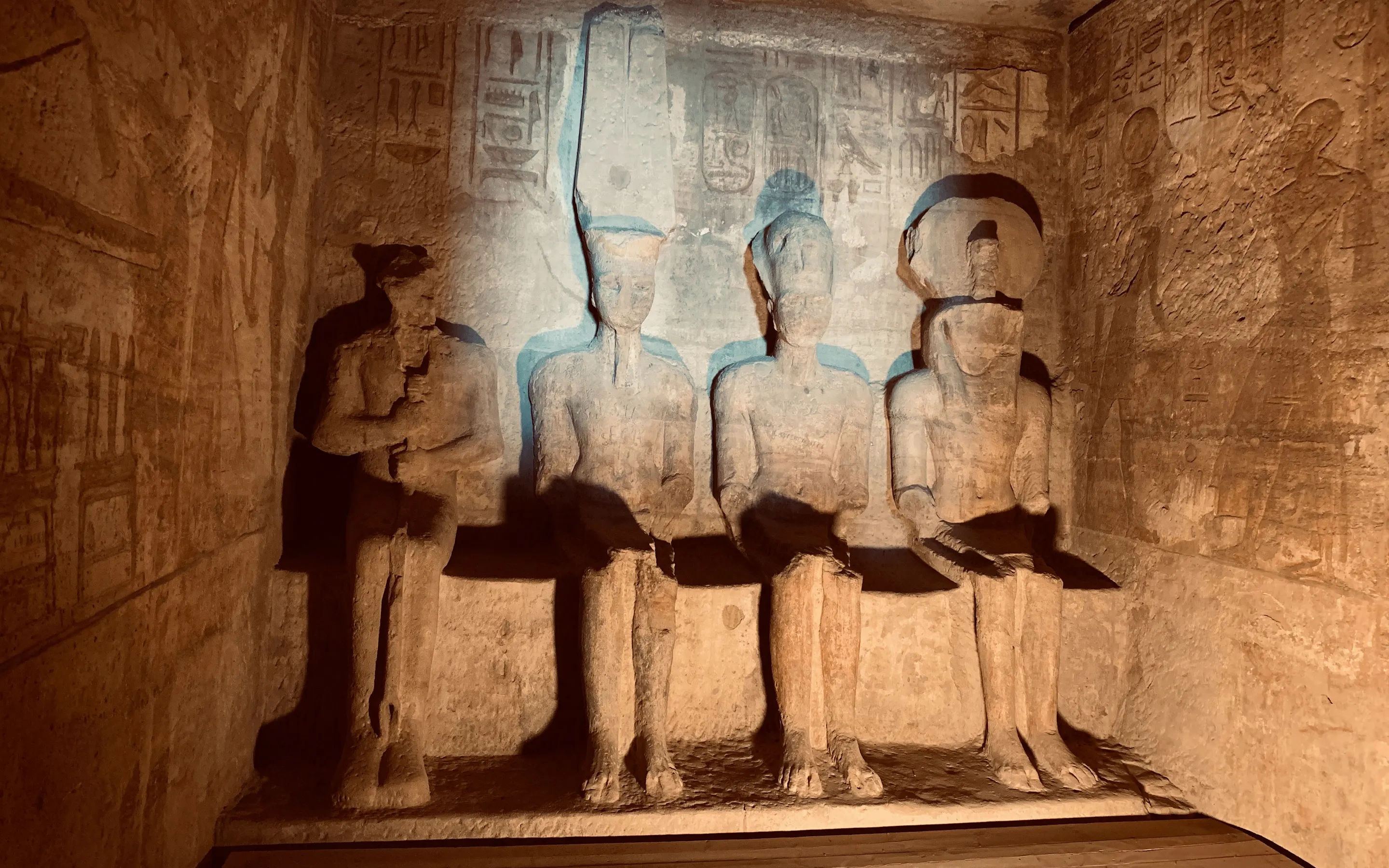 Four carved figures sit inside a dim stone chamber at Karnak in Luxor, with etched walls and warm spotlighted reliefs.