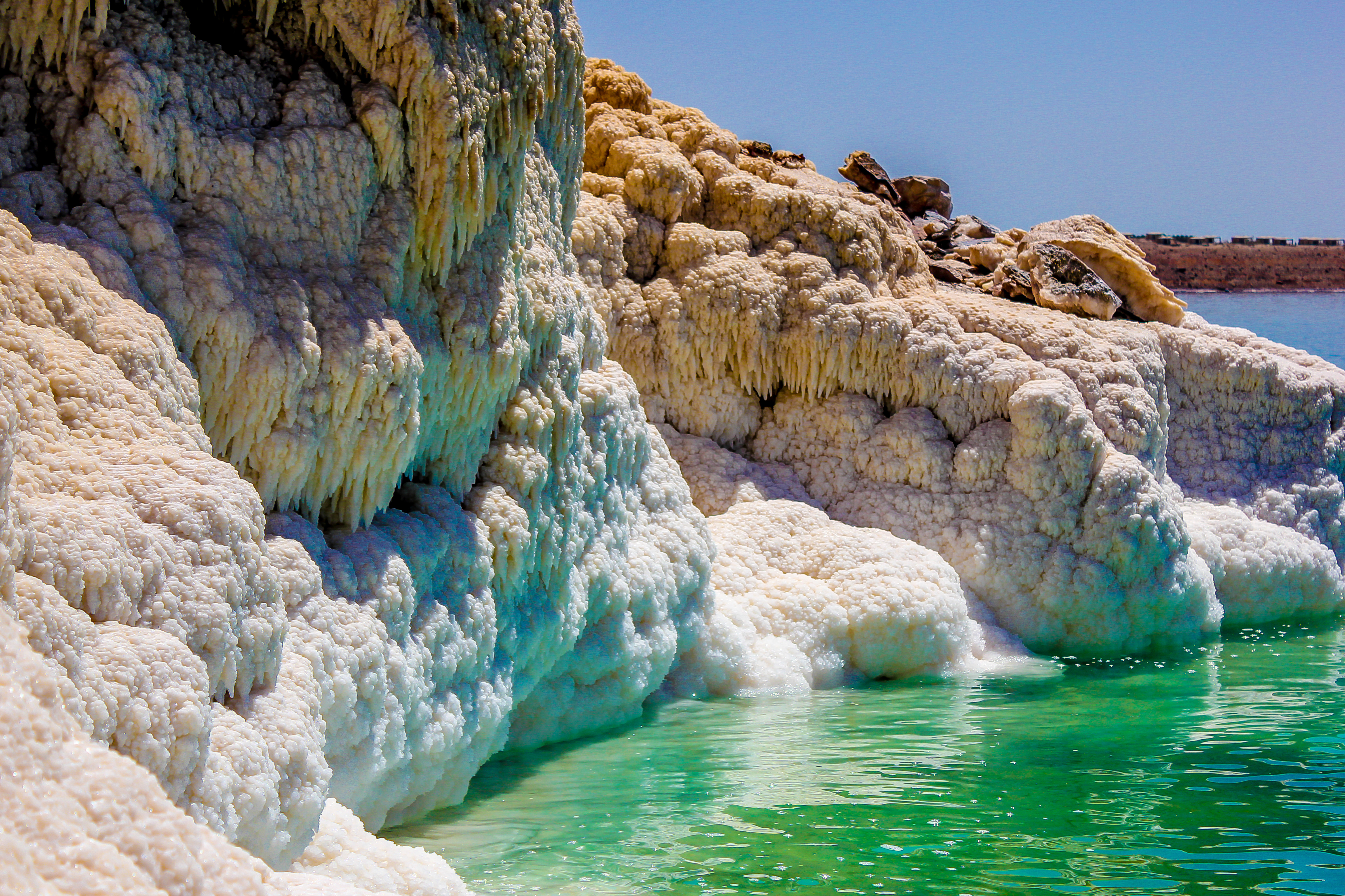 White salt formations cascade into bright turquoise water along the rocky shoreline of the Dead Sea in Jordan.