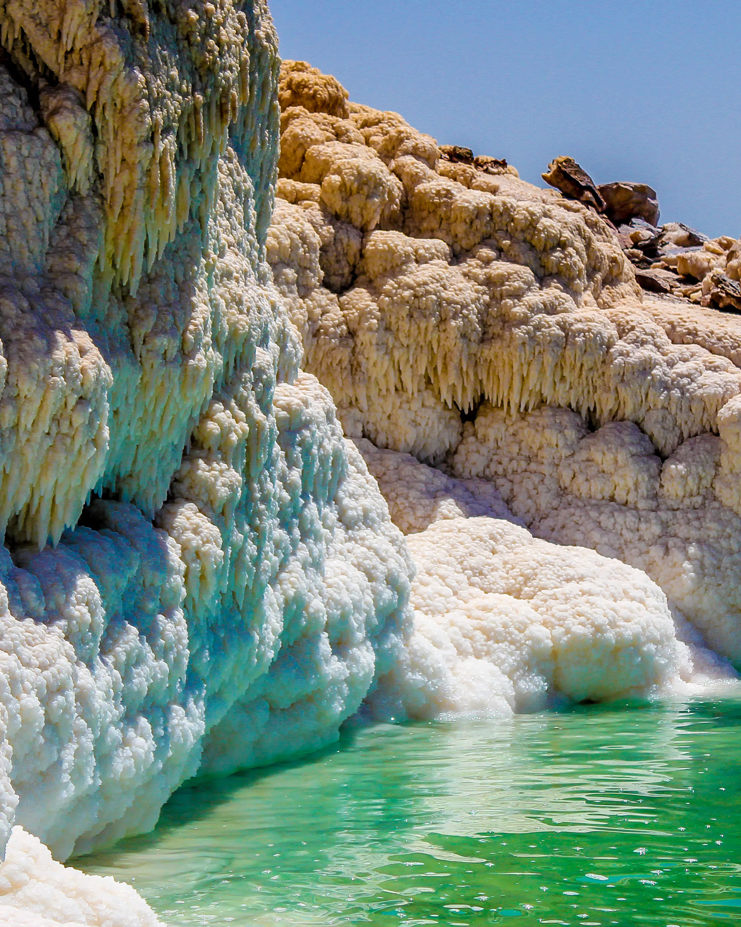 White salt formations cascade into bright turquoise water along the rocky shoreline of the Dead Sea in Jordan.