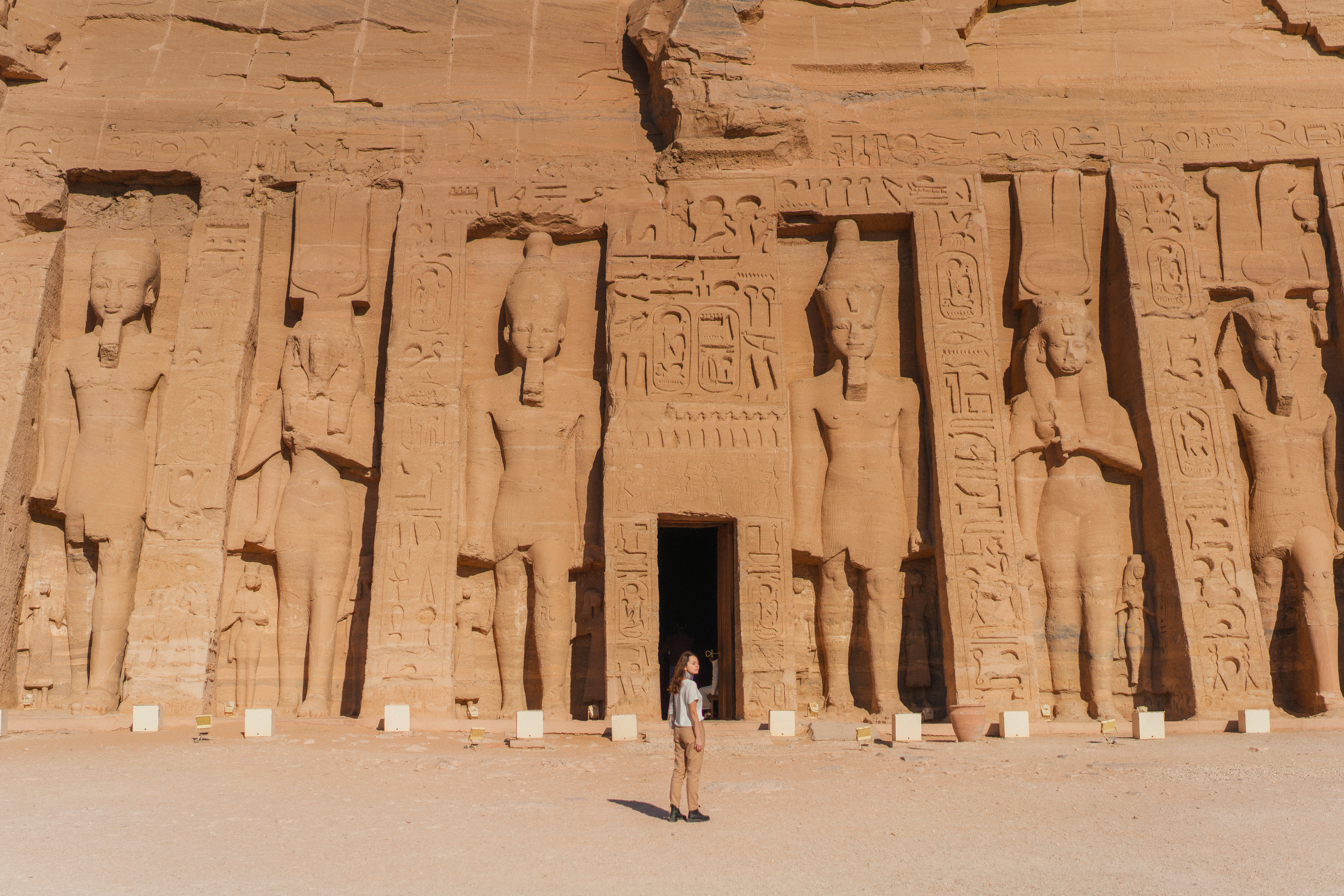 One visitor stands before the towering carved façade of Abu Simbel, framed by colossal statues and desert sand.