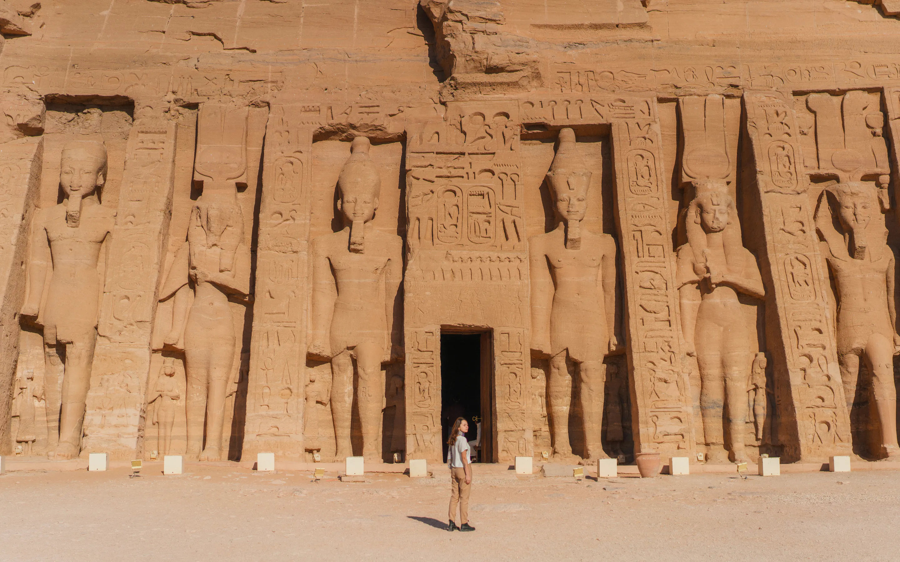 One visitor stands before the towering carved façade of Abu Simbel, framed by colossal statues and desert sand.