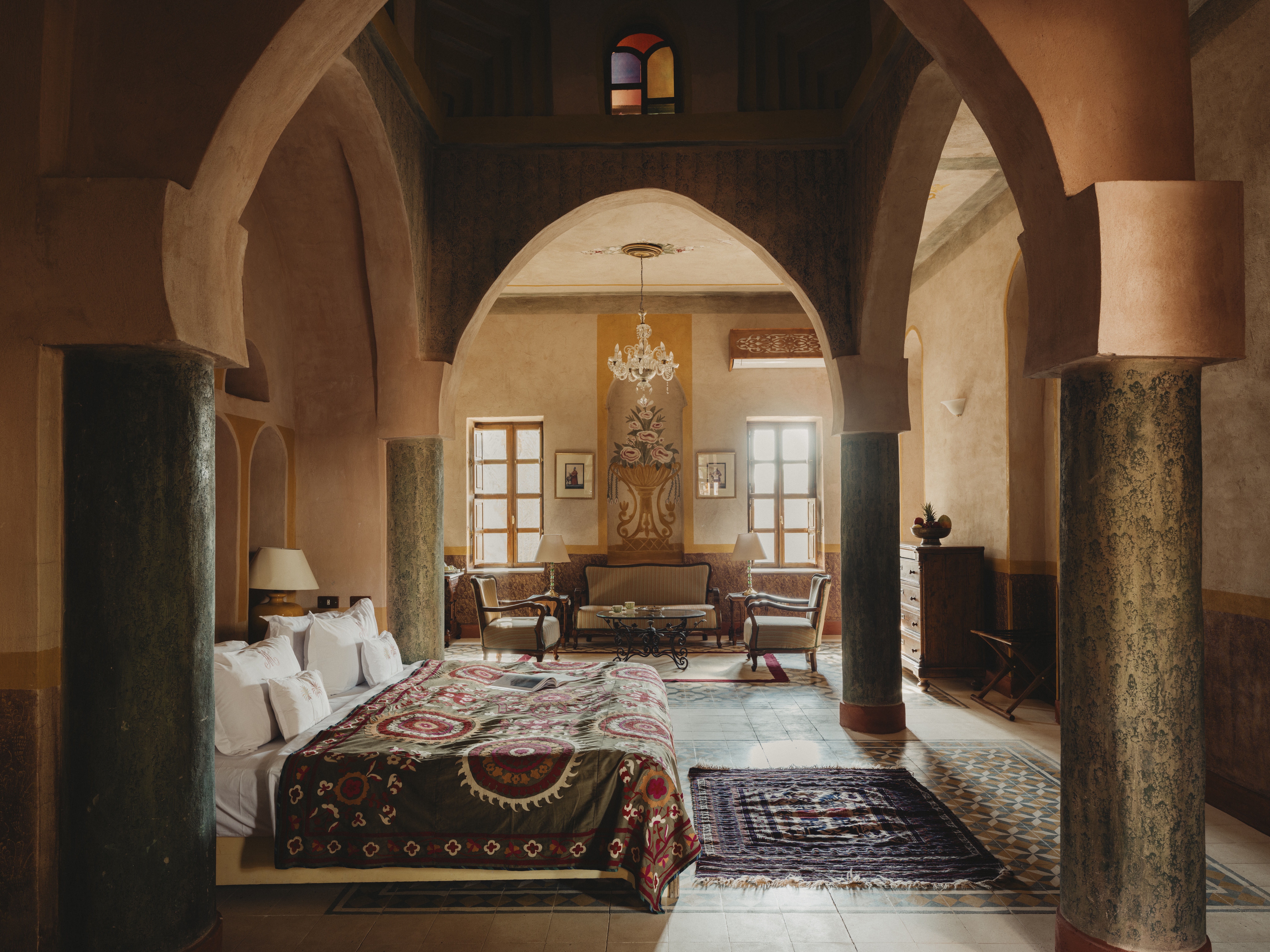 A high-arched bedroom at Al Moudira Hotel features painted columns, a patterned bedspread, and a bright seating area.
