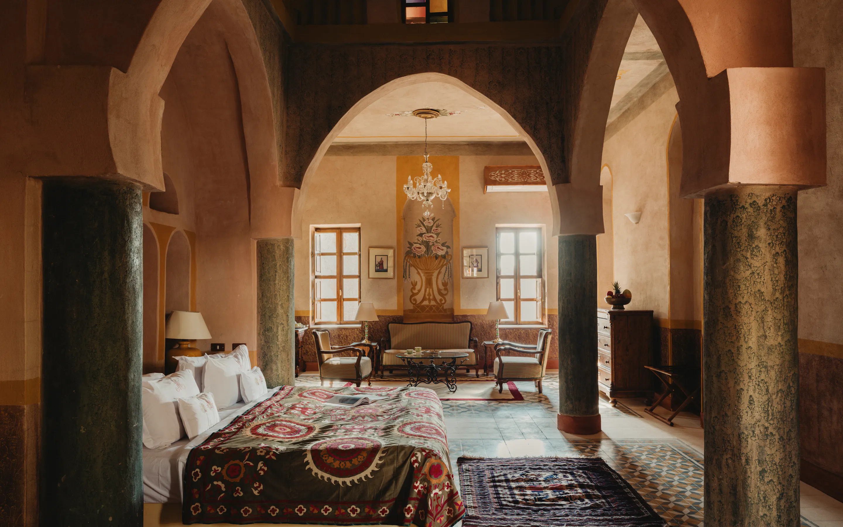 A high-arched bedroom at Al Moudira Hotel features painted columns, a patterned bedspread, and a bright seating area.