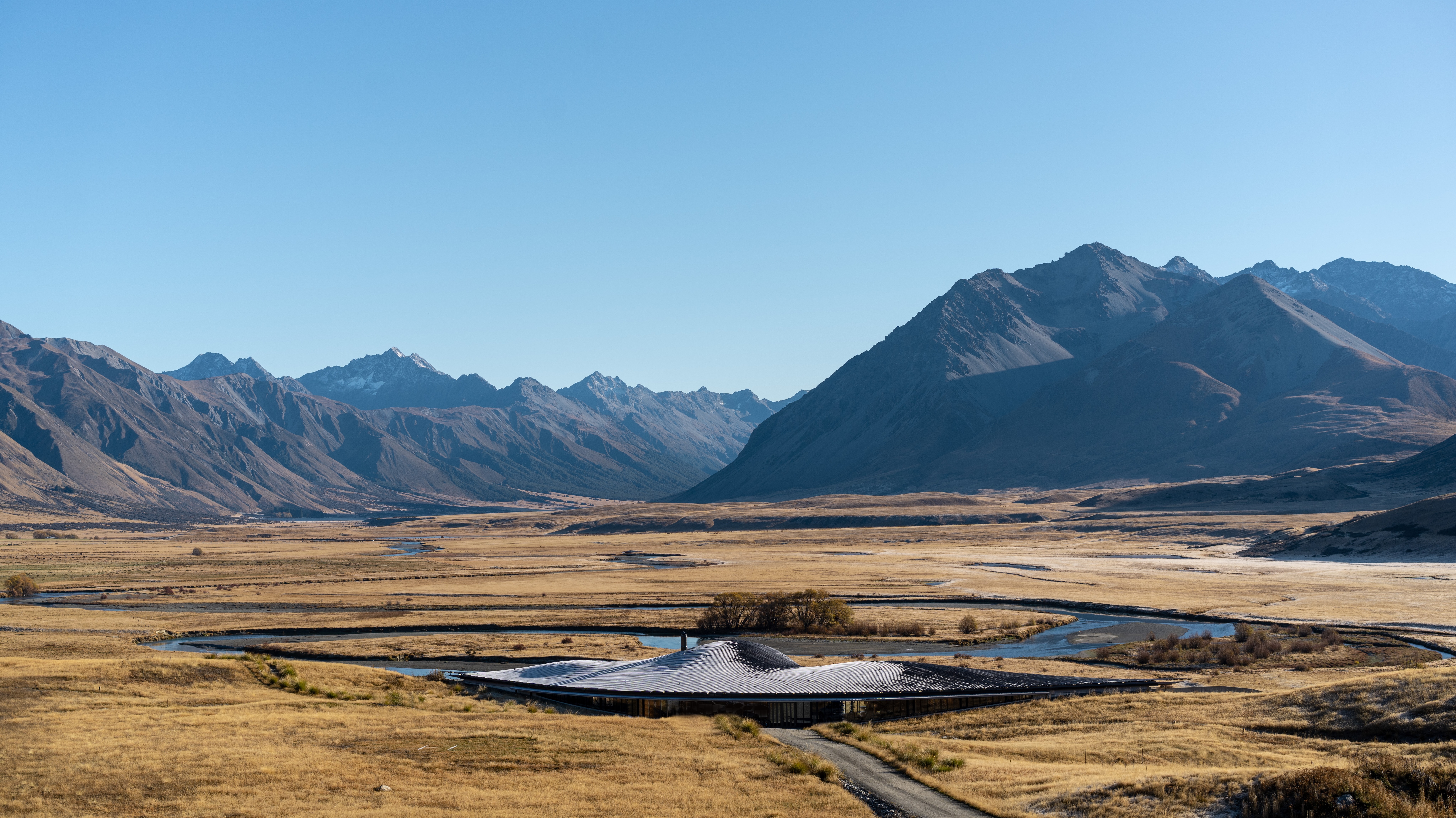 The Lindis Lodge sits low in a broad alpine valley, with braided streams and rugged mountains stretching behind it.