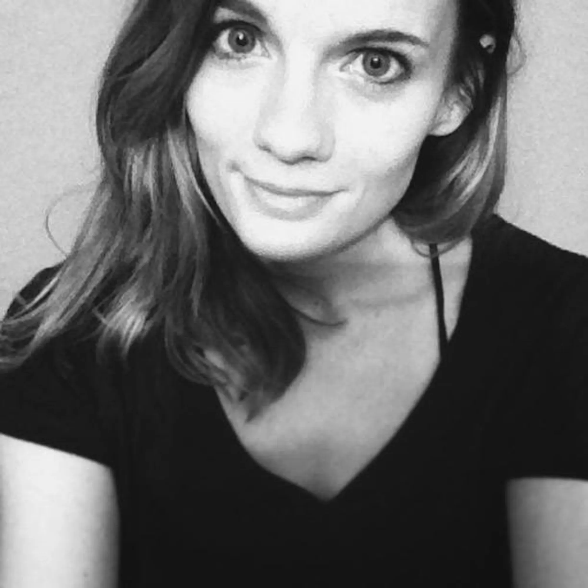 A woman with brown hair wearing a black t-shirt smiles at the camera. 