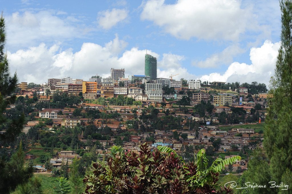 Kigali's hillside skyline rises above layered neighborhoods and trees beneath bright clouds in Rwanda's capital.