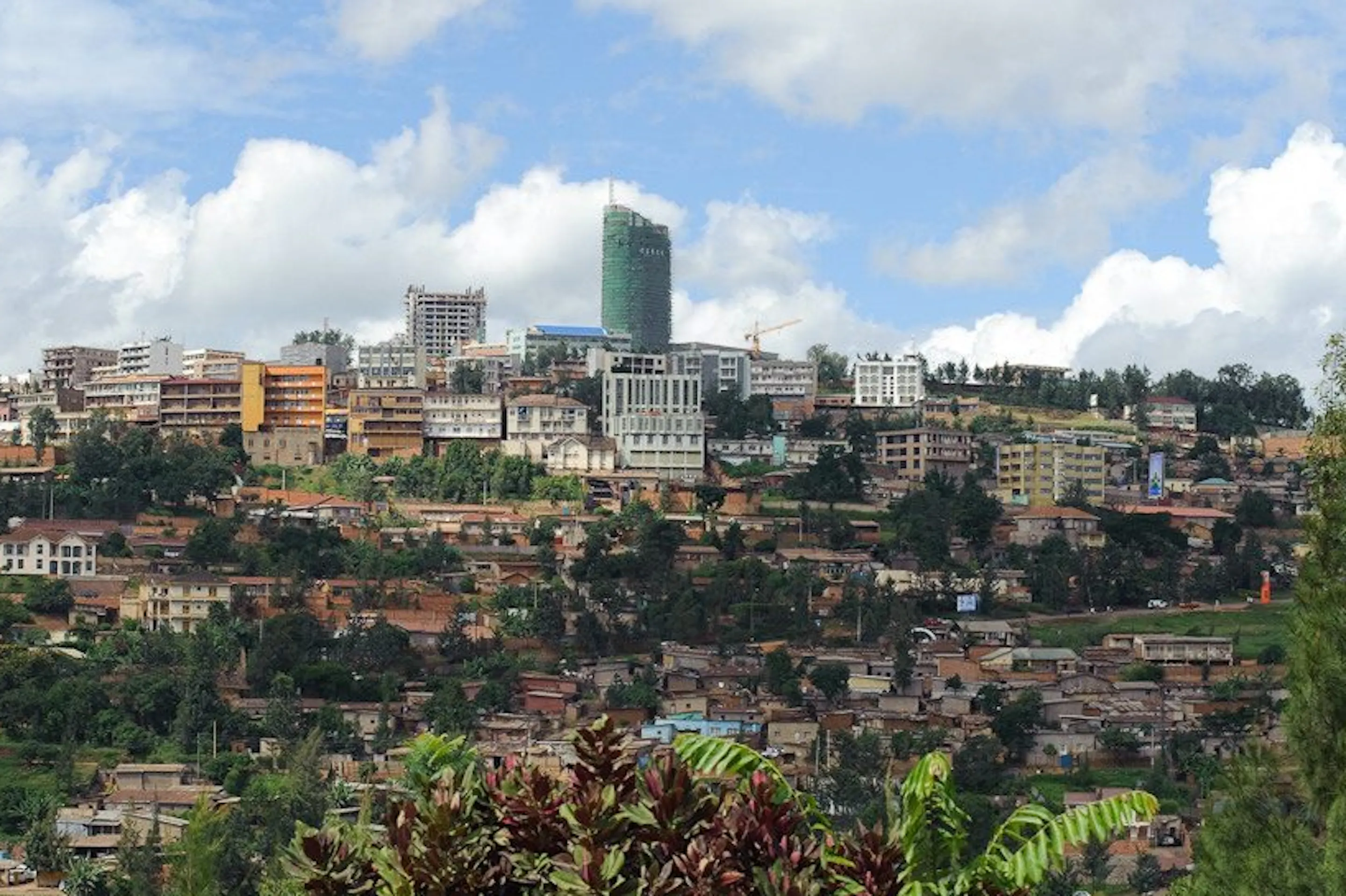 Kigali's hillside skyline rises above layered neighborhoods and trees beneath bright clouds in Rwanda's capital.