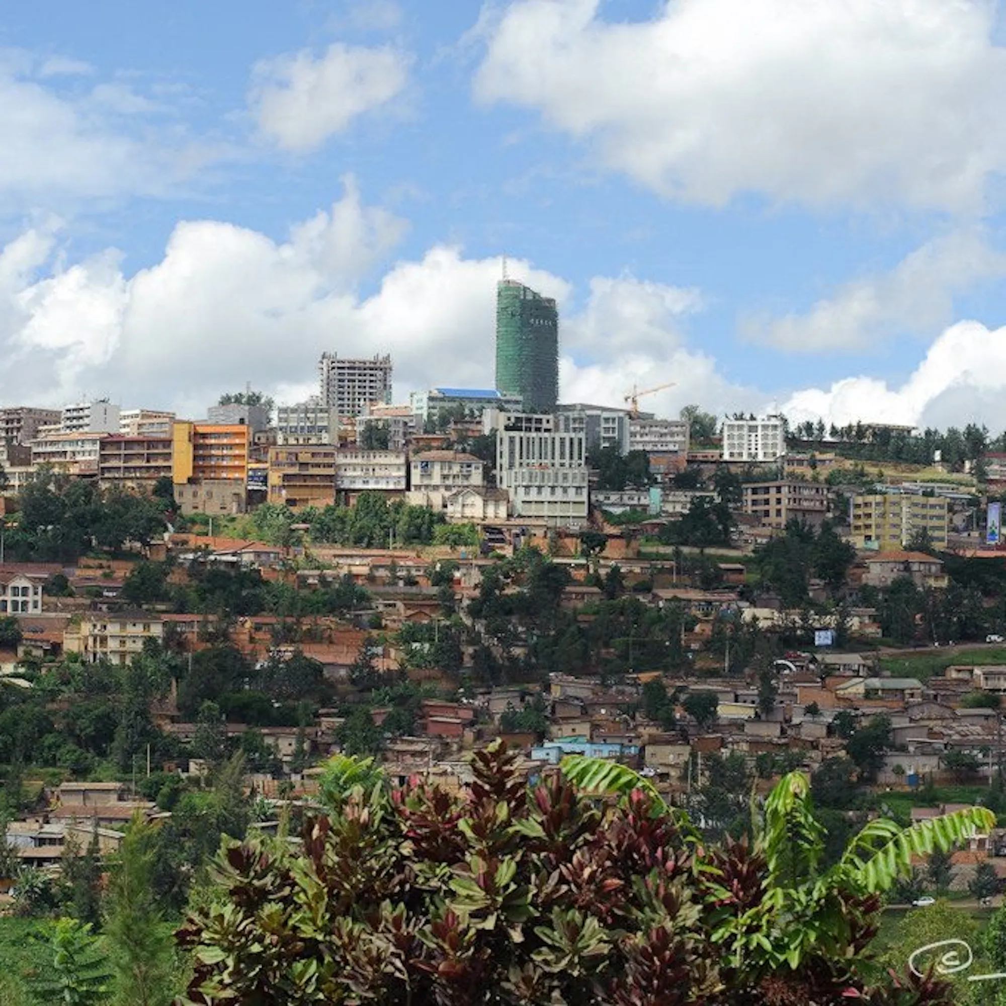 Kigali's hillside skyline rises above layered neighborhoods and trees beneath bright clouds in Rwanda's capital.