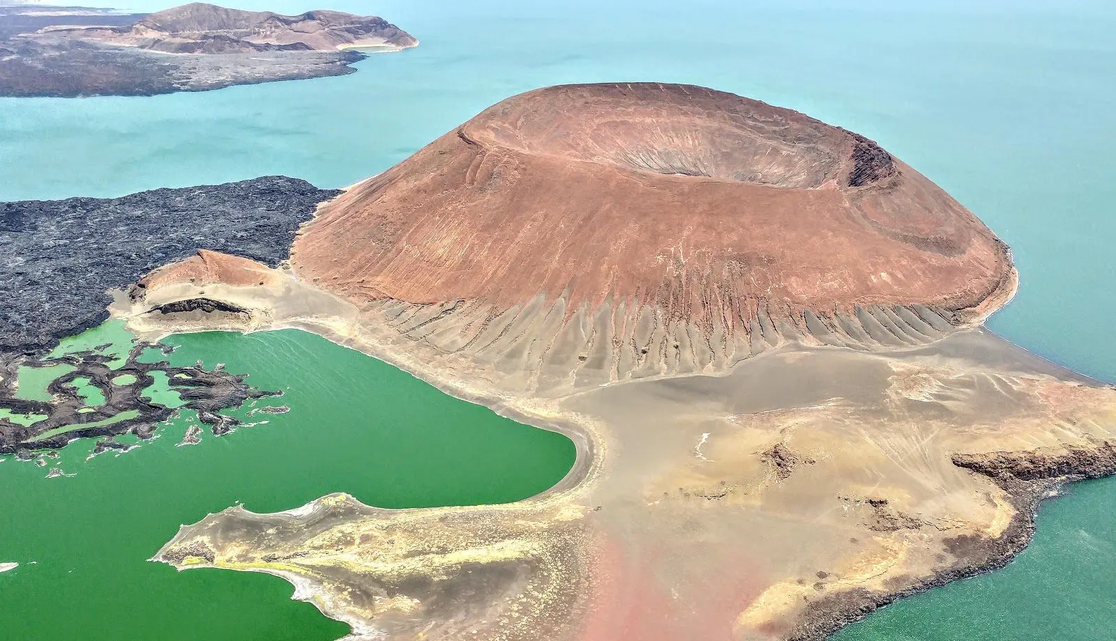 Volcanic Nabuyatom cone rises from Lake Turkana's jade water, with black lava fields and pale shoreline below.