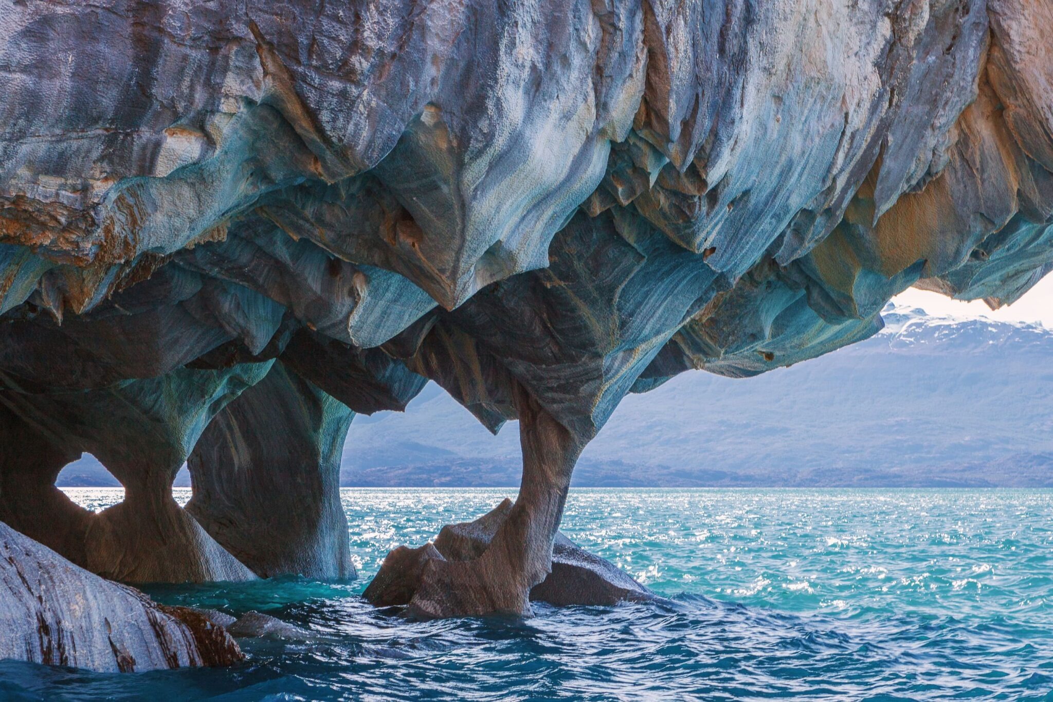 Swirling blue rock arches rise above clear water at the Marble Caves in Chile's Aysén region under soft light.