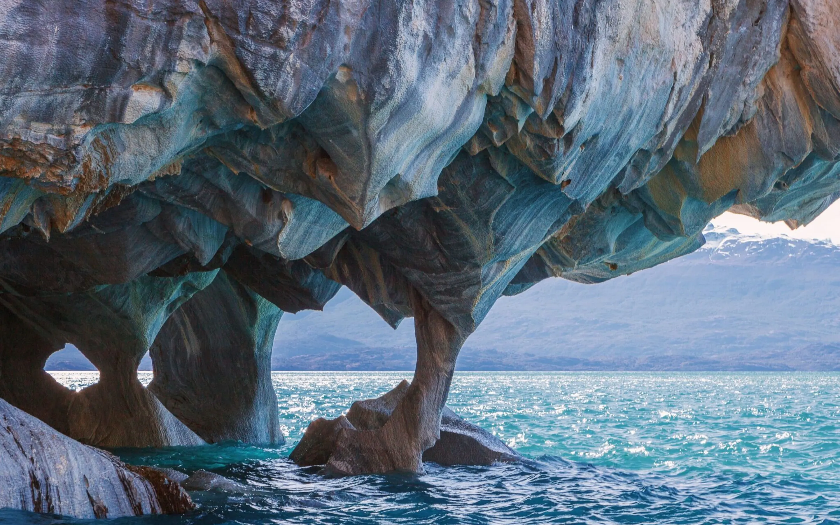 Swirling blue rock arches rise above clear water at the Marble Caves in Chile's Aysén region under soft light.