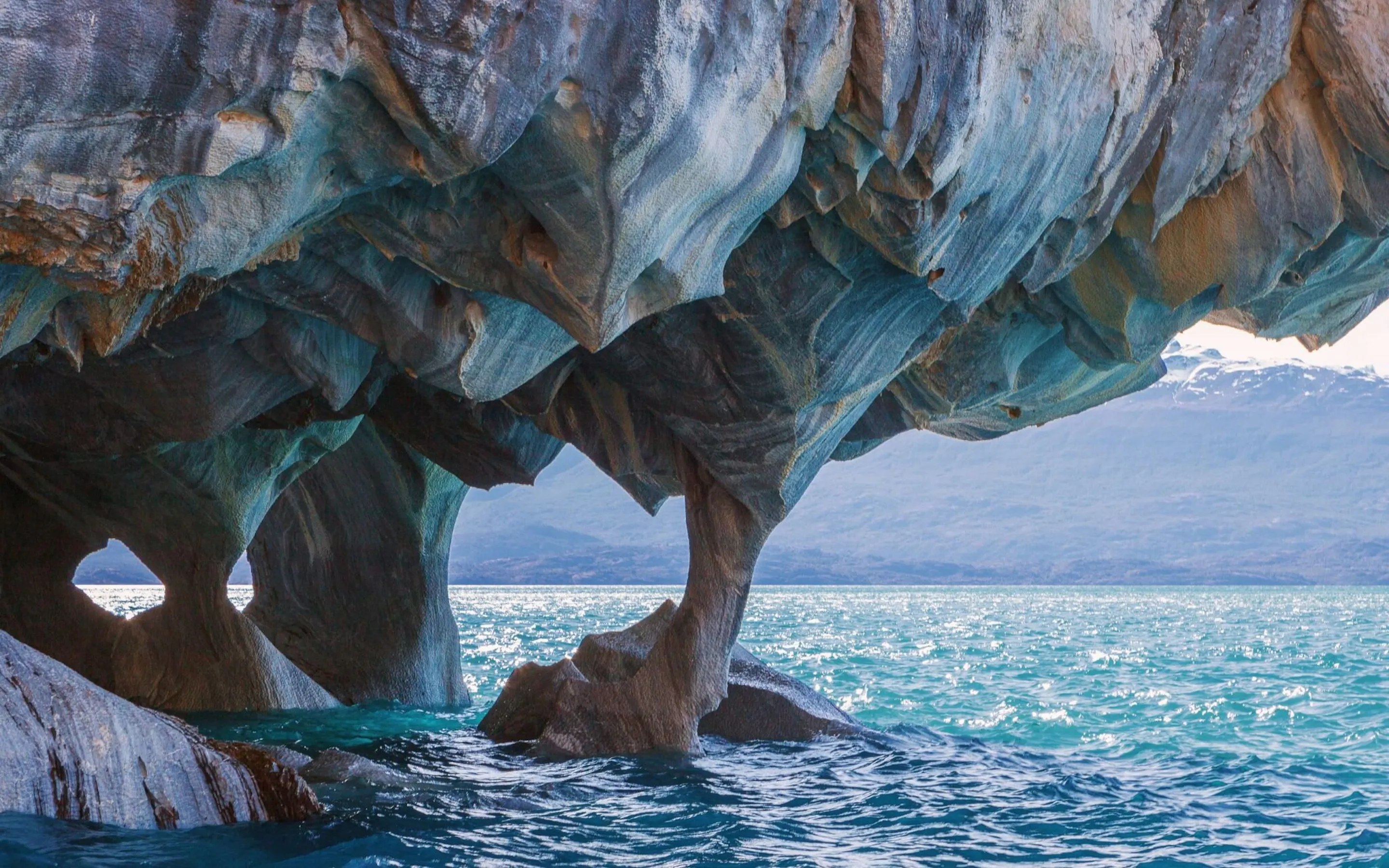 Swirling blue rock arches rise above clear water at the Marble Caves in Chile's Aysén region under soft light.