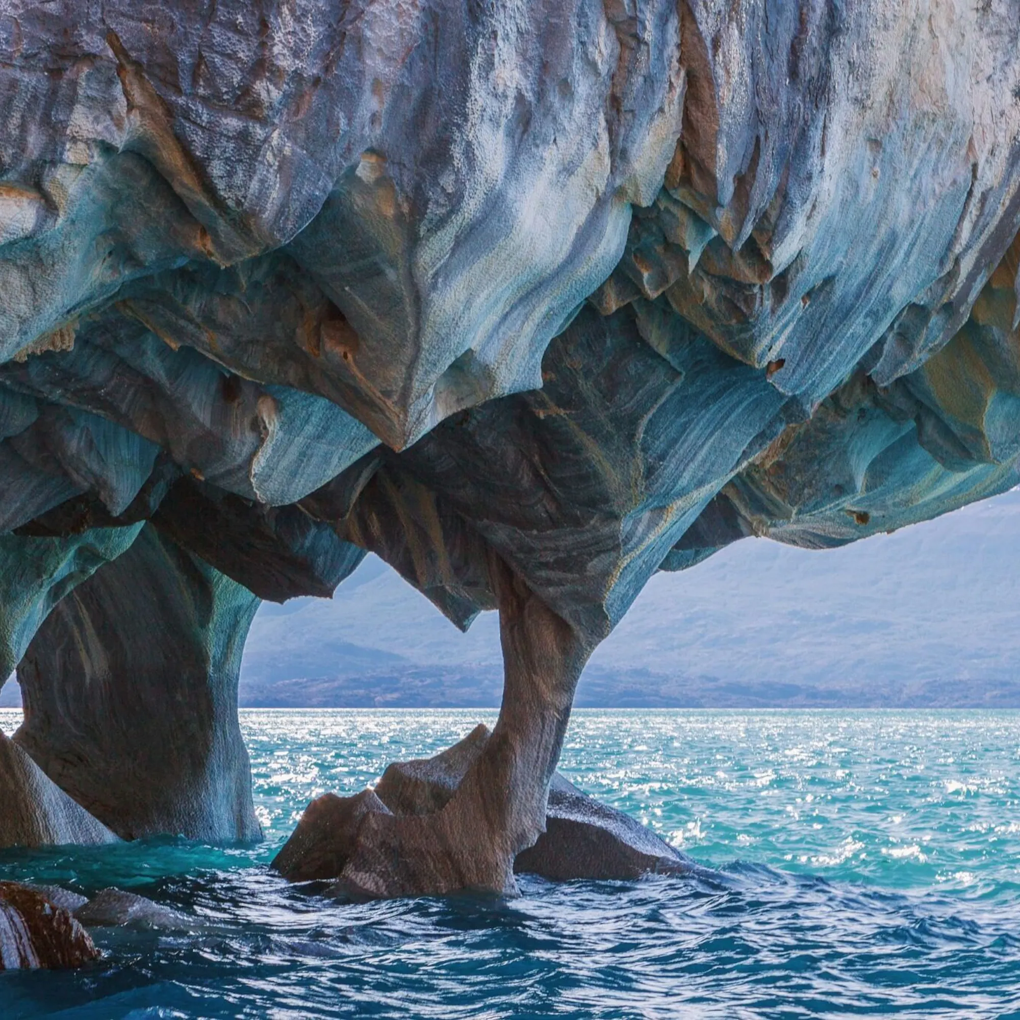 Swirling blue rock arches rise above clear water at the Marble Caves in Chile's Aysén region under soft light.