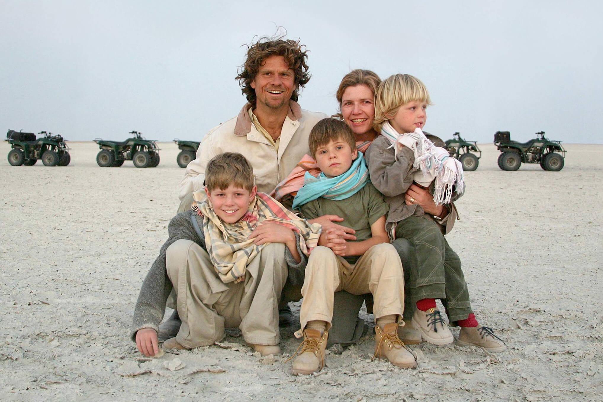 A family sits together on open salt flats with a line of quad bikes behind them during a safari stop in Botswana.