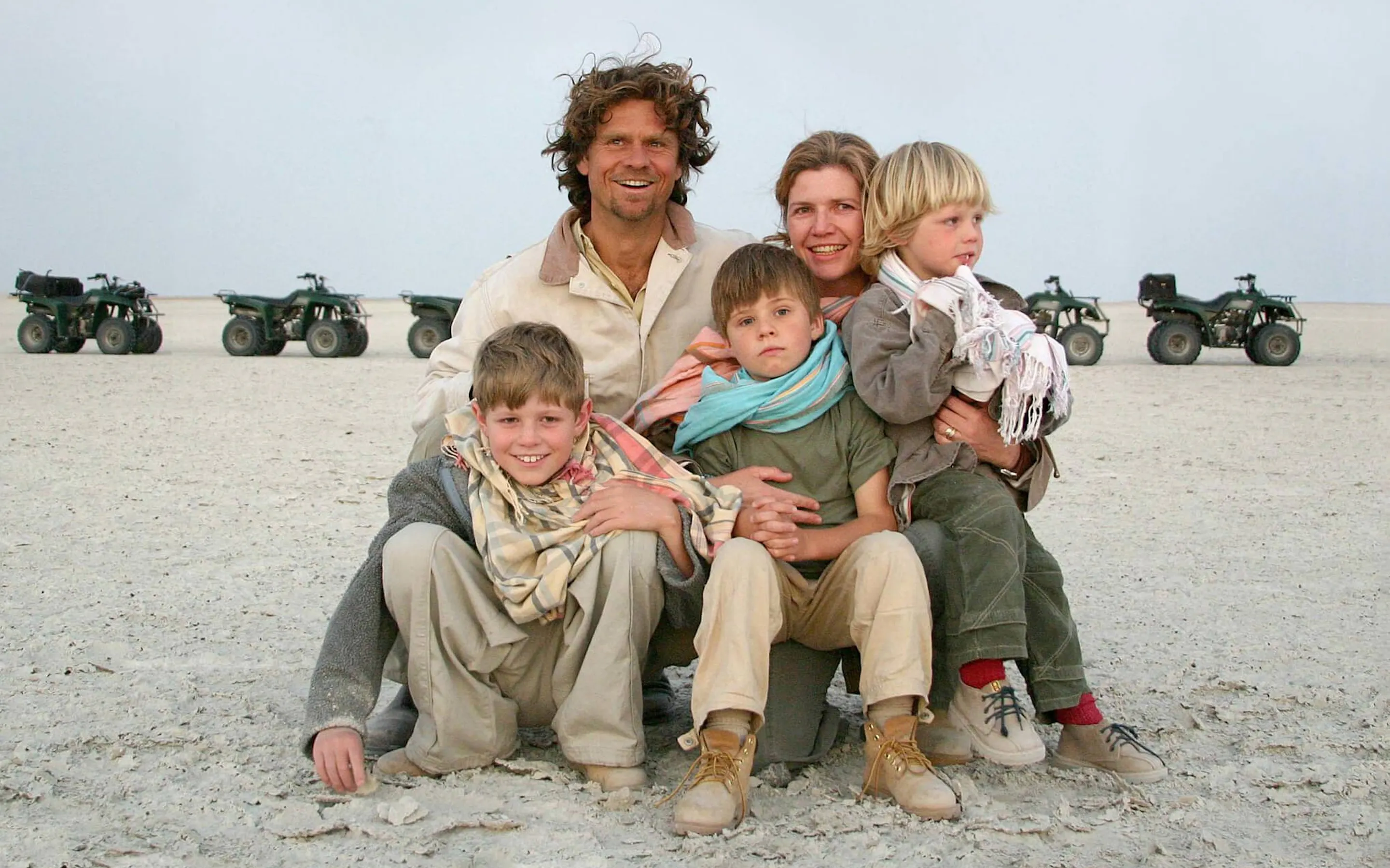 A family sits together on open salt flats with a line of quad bikes behind them during a safari stop in Botswana.