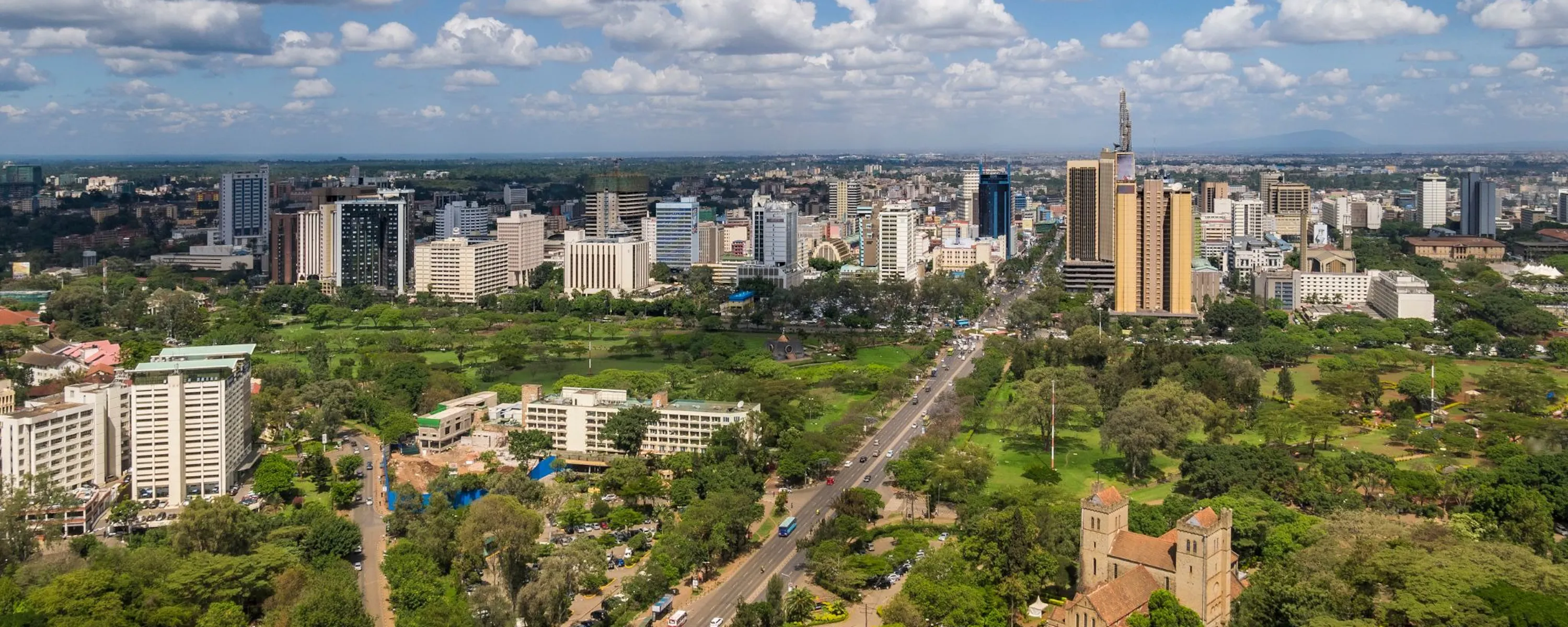 Nairobi's skyline stretches beyond a wide avenue, green parks, and a church beneath scattered clouds in Kenya.