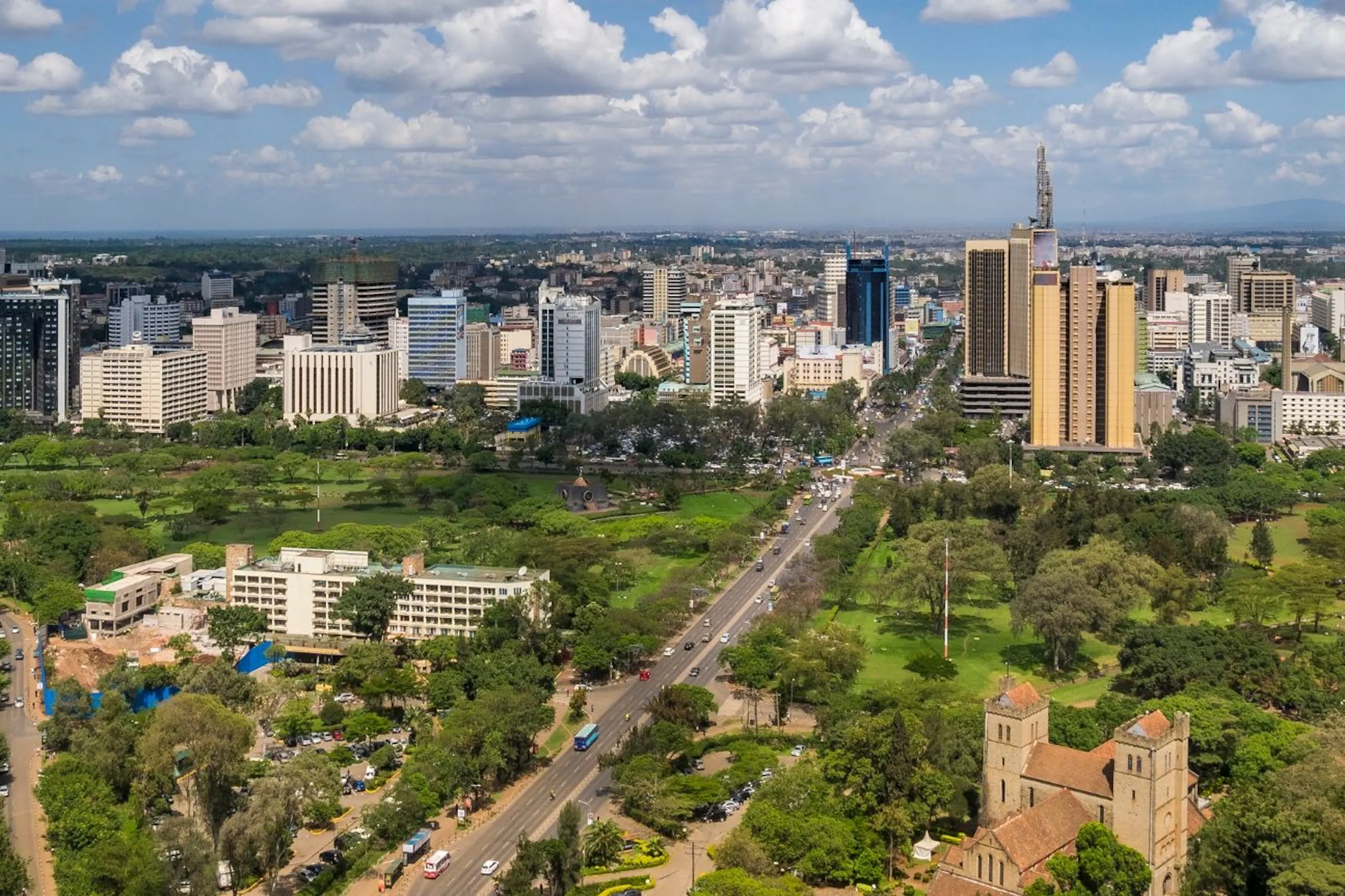 Nairobi's skyline stretches beyond a wide avenue, green parks, and a church beneath scattered clouds in Kenya.