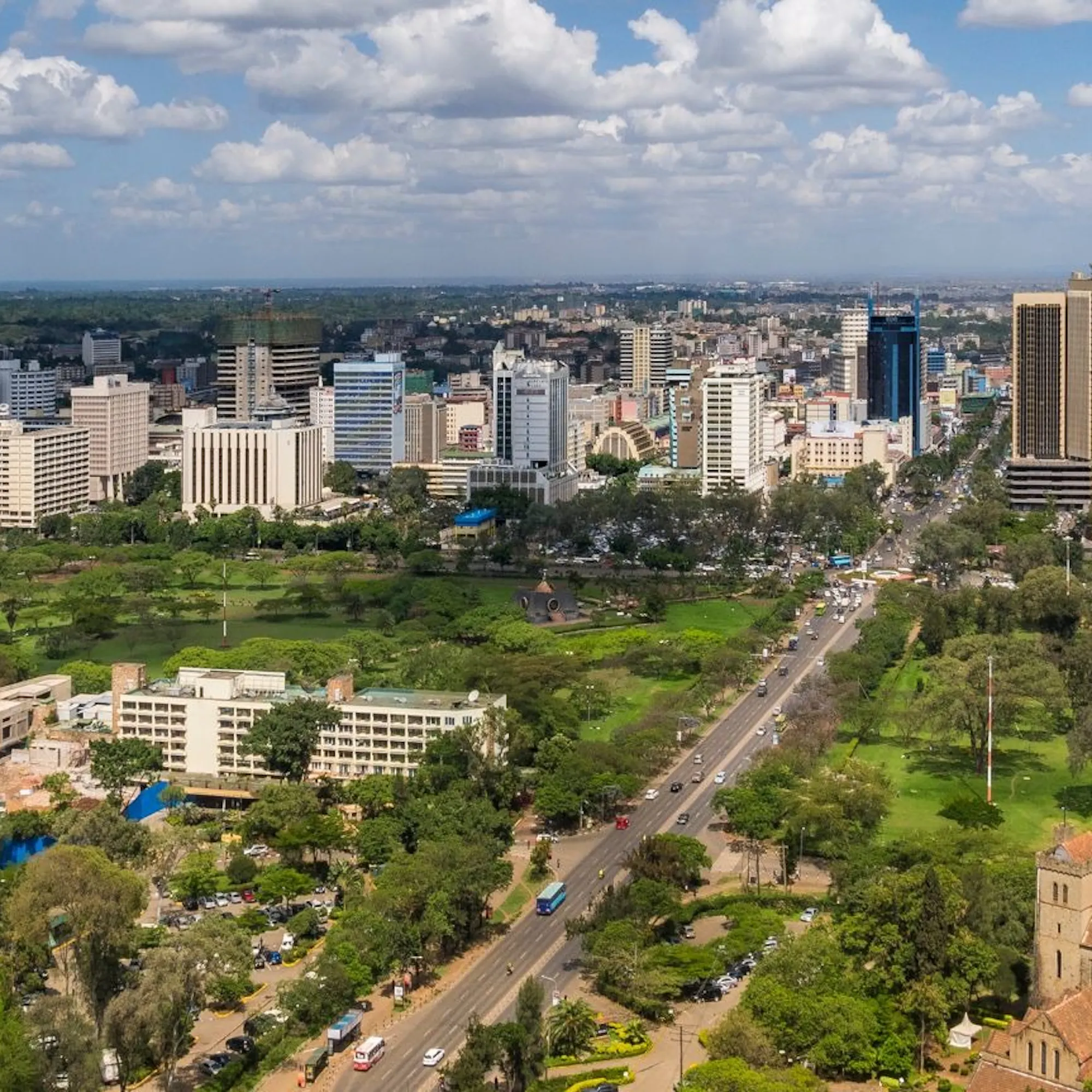 Nairobi's skyline stretches beyond a wide avenue, green parks, and a church beneath scattered clouds in Kenya.