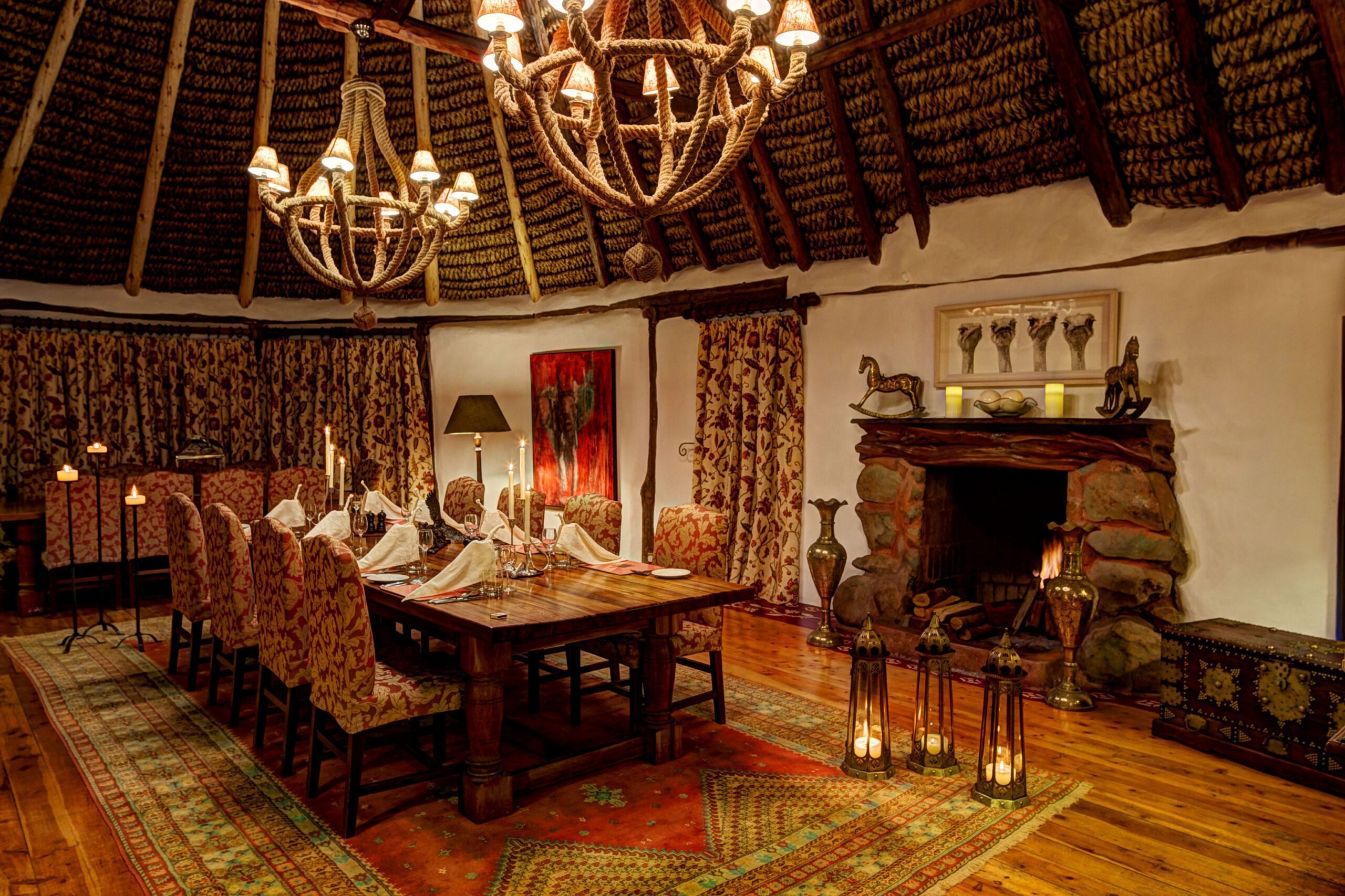 A candlelit dining room at Laragai House features chandeliers, patterned rugs, and a fireplace in Laikipia, Kenya.