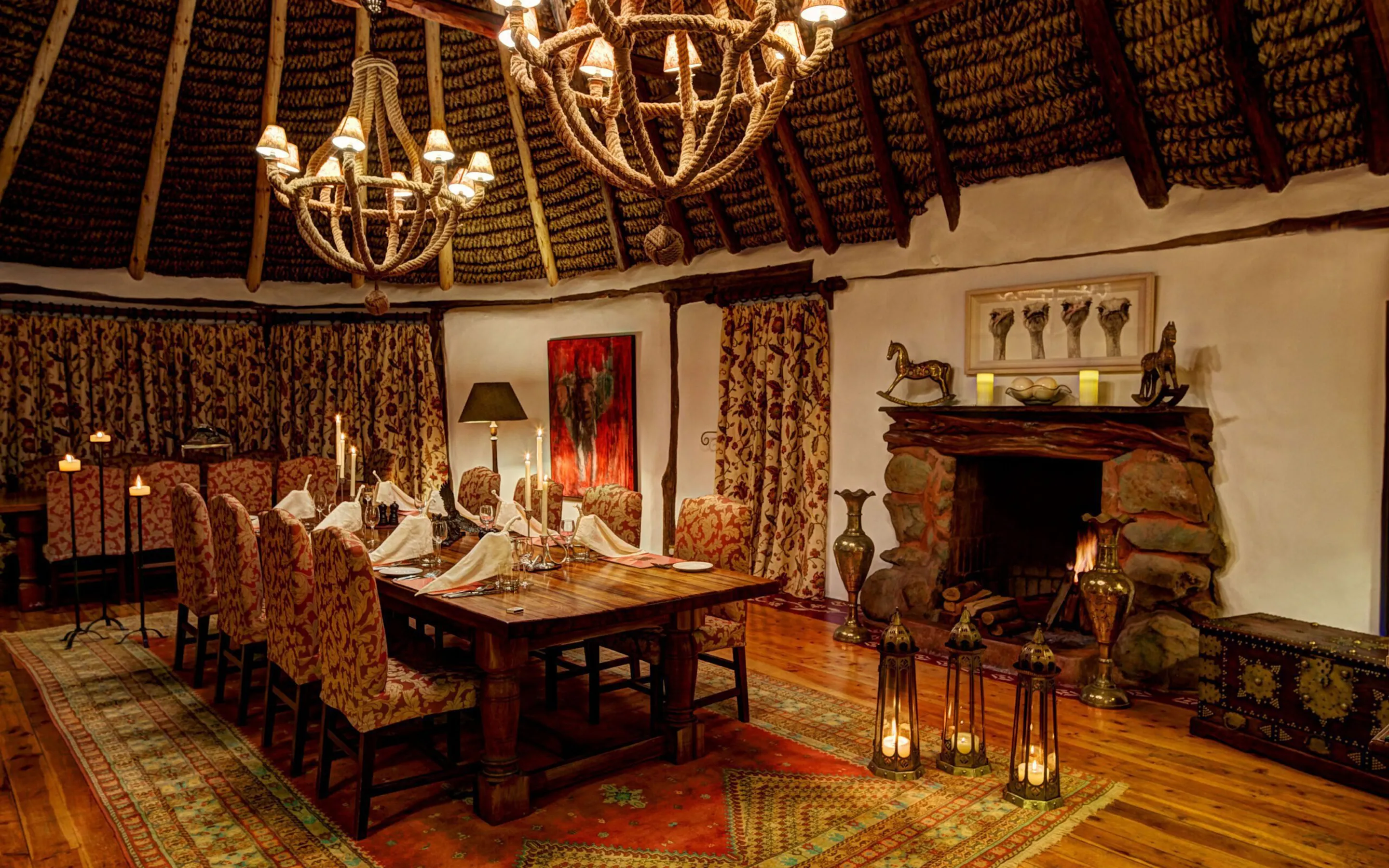 A candlelit dining room at Laragai House features chandeliers, patterned rugs, and a fireplace in Laikipia, Kenya.