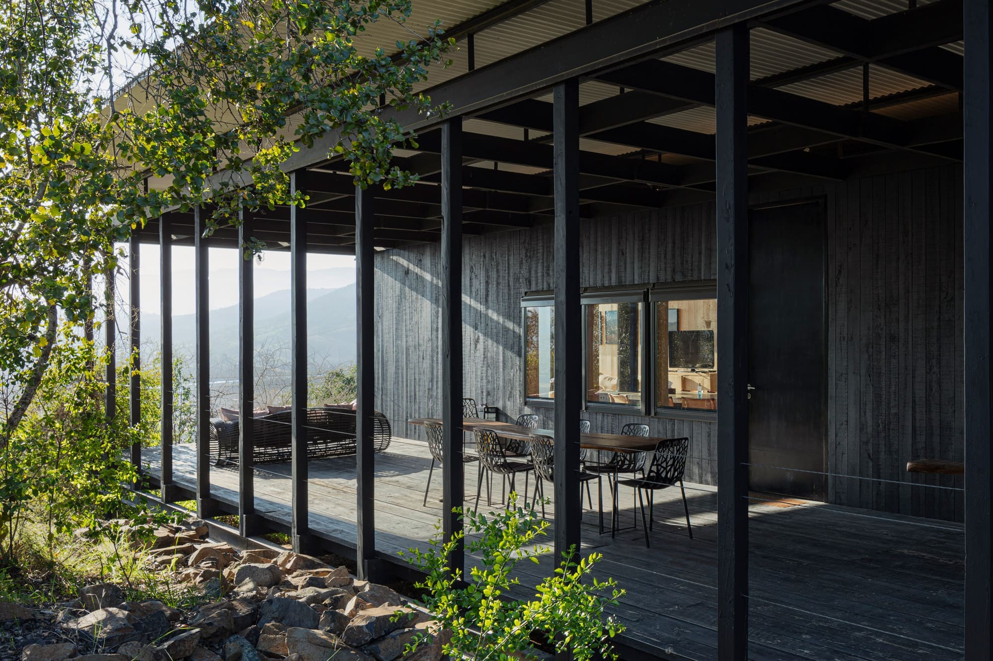A shaded timber terrace with dining tables overlooks hazy mountain views at Vik Chile in the Cachapoal Valley.