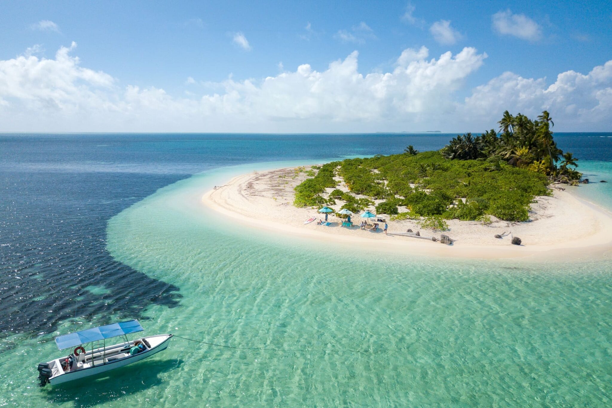 A boat floats beside shallow turquoise water and a white sandbank fringed with greenery near Alphonse Island.