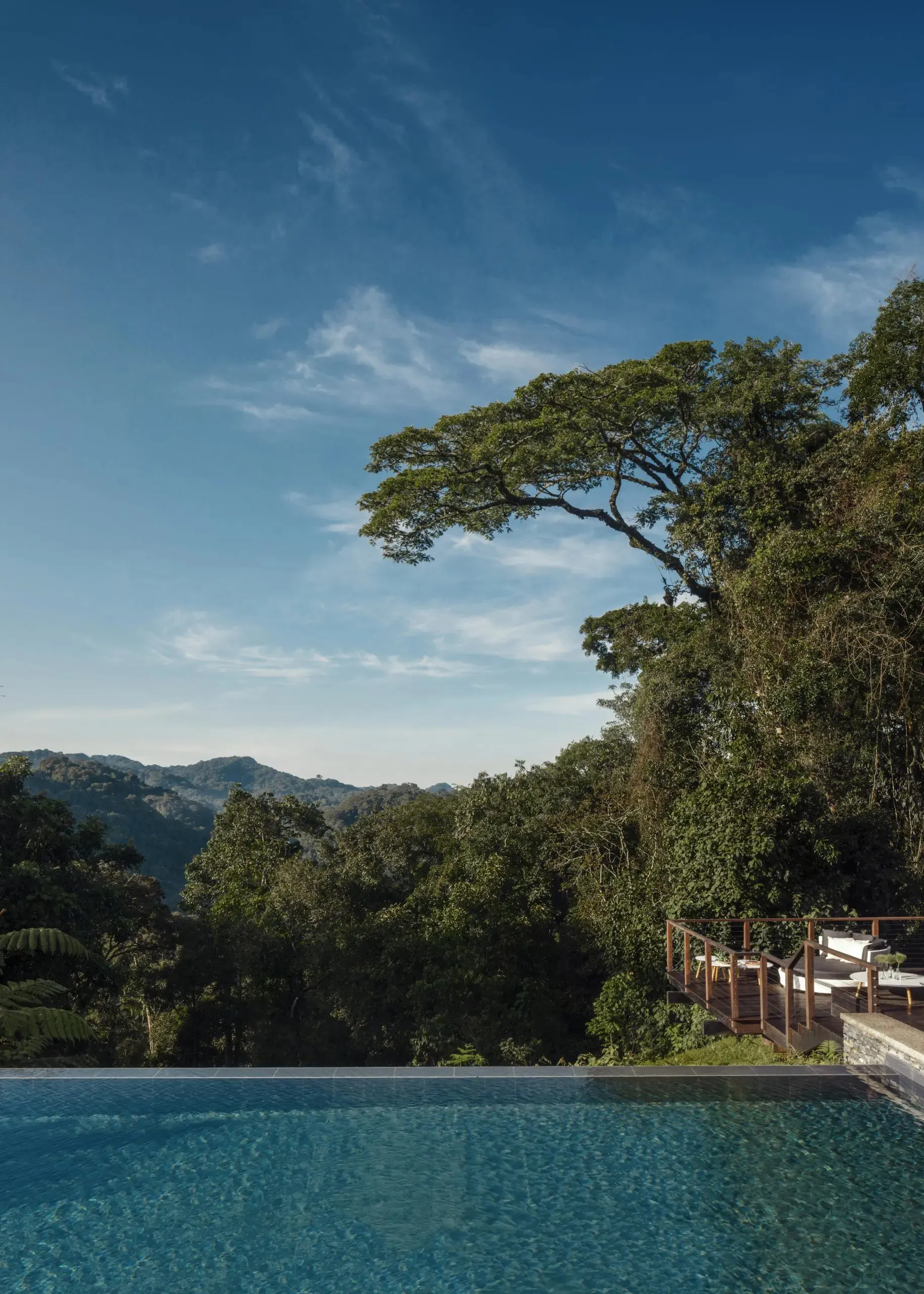 An infinity pool at One&Only Nyungwe House looks across water toward forested hills and a bright blue sky in Rwanda.