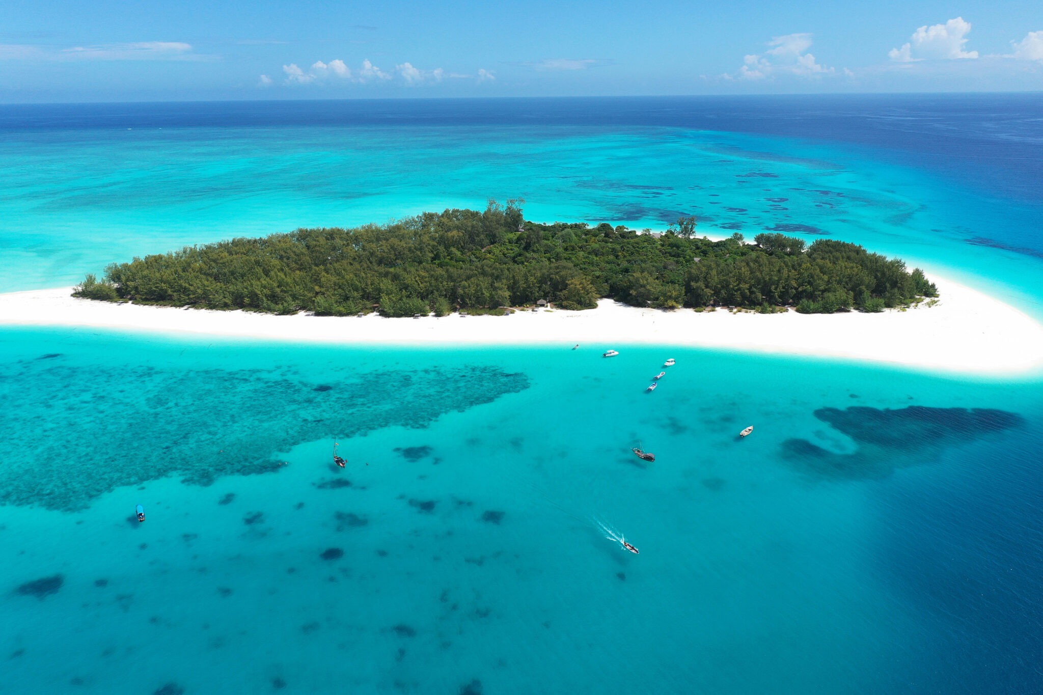Mnemba Island sits within bright turquoise water, with white sand, coral patches, and boats offshore in Tanzania.